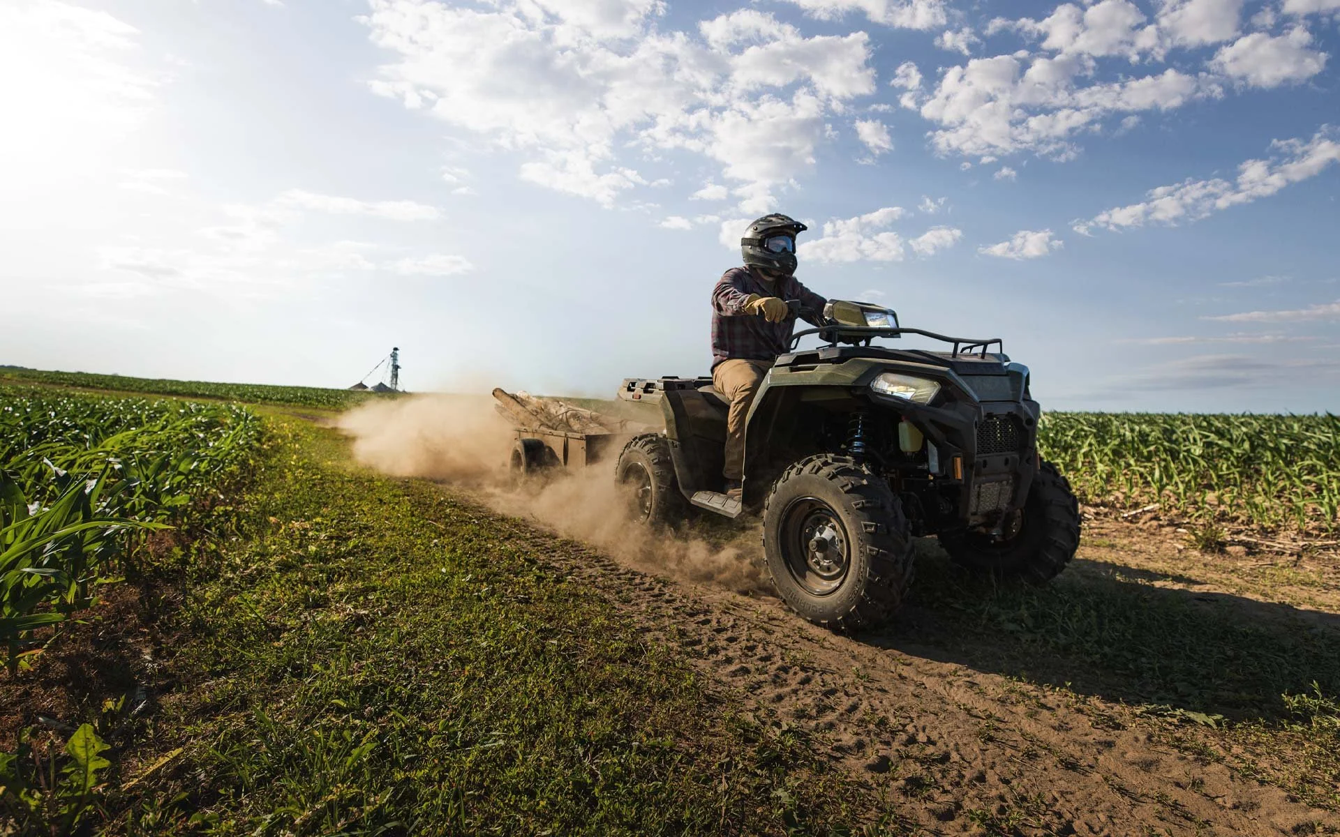 Person som kör Polaris Sportsman 570 på en jordbruksväg i ett fält under en molnig himmel.