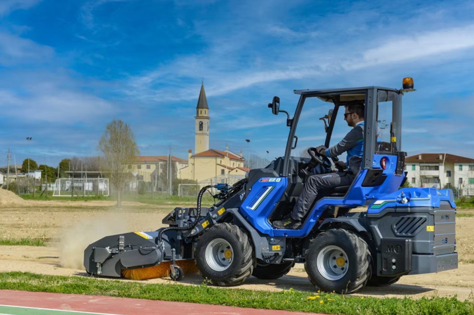 En man kör en MultiOne  på en byggarbetsplats medan den sopar bort damm och gräs.