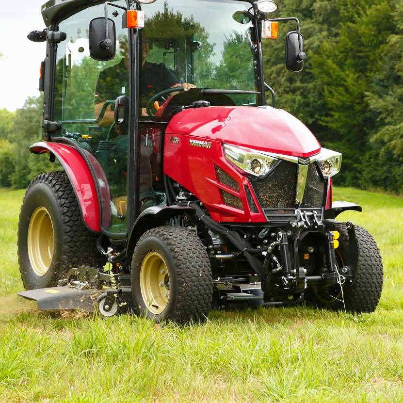 En röd Yanmar traktor med kabin och stora däck står på en gräsmatta med träd i bakgrunden.