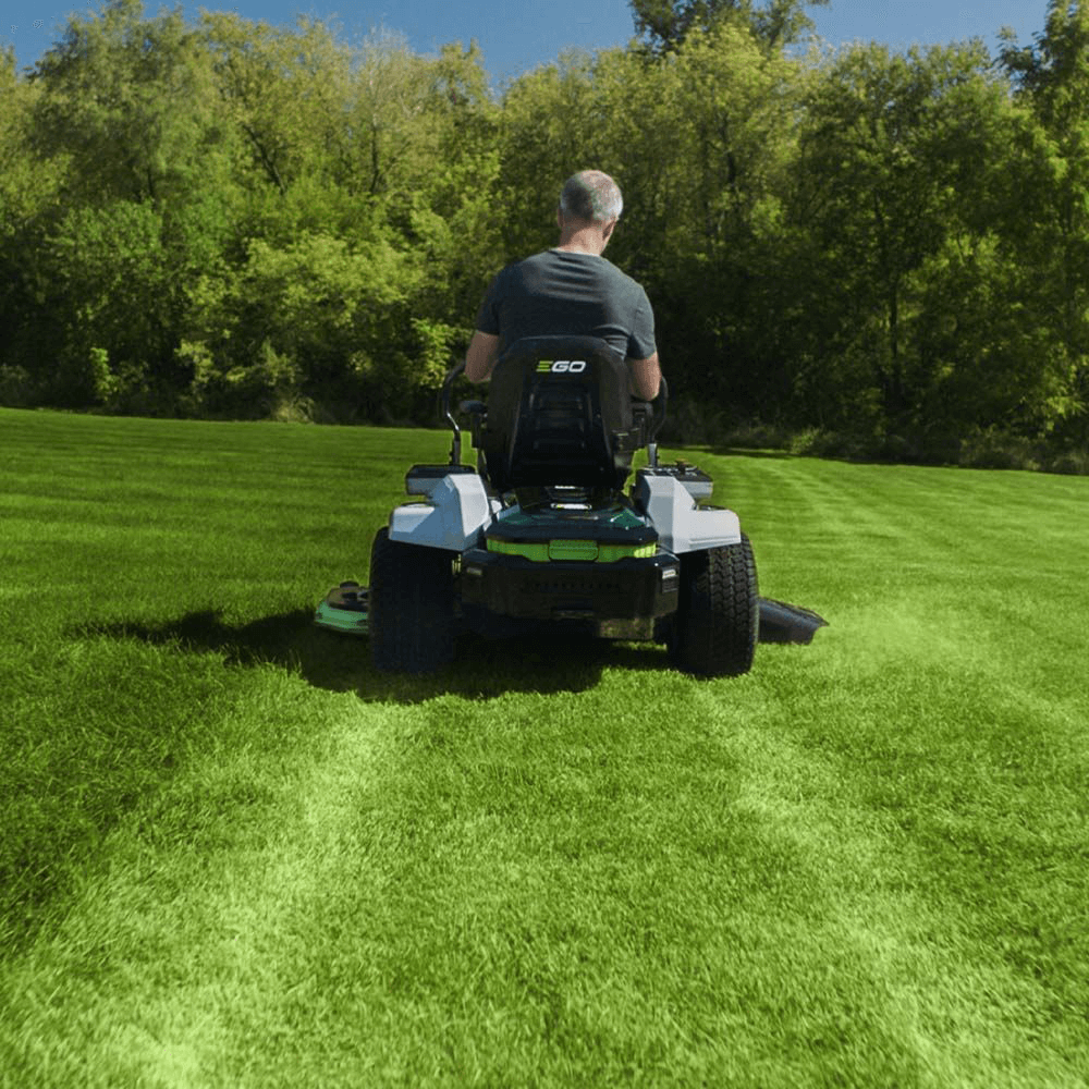 En person som kör en EGO Z6 på en backig gräsmatta med träd i bakgrunden.