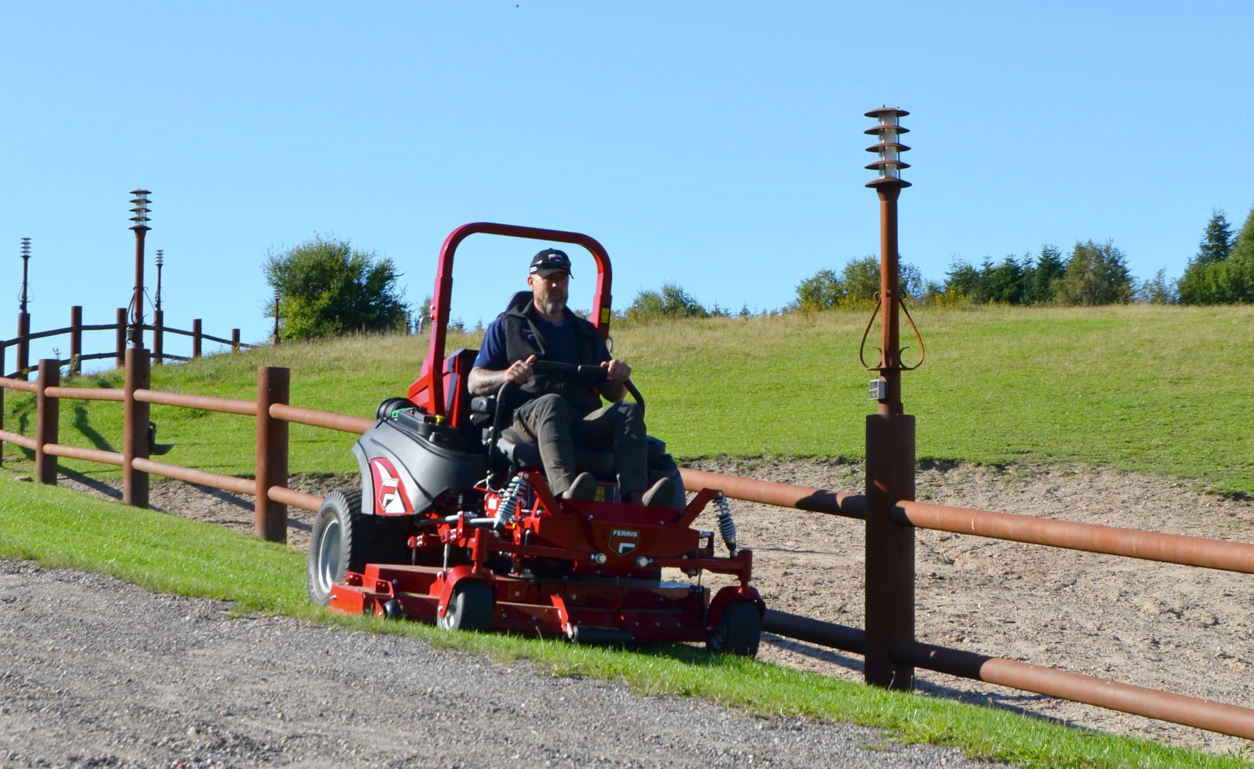 Man i blå tröja och keps kör en Ferris på gräsmatta med radhus och träd i bakgrunden.