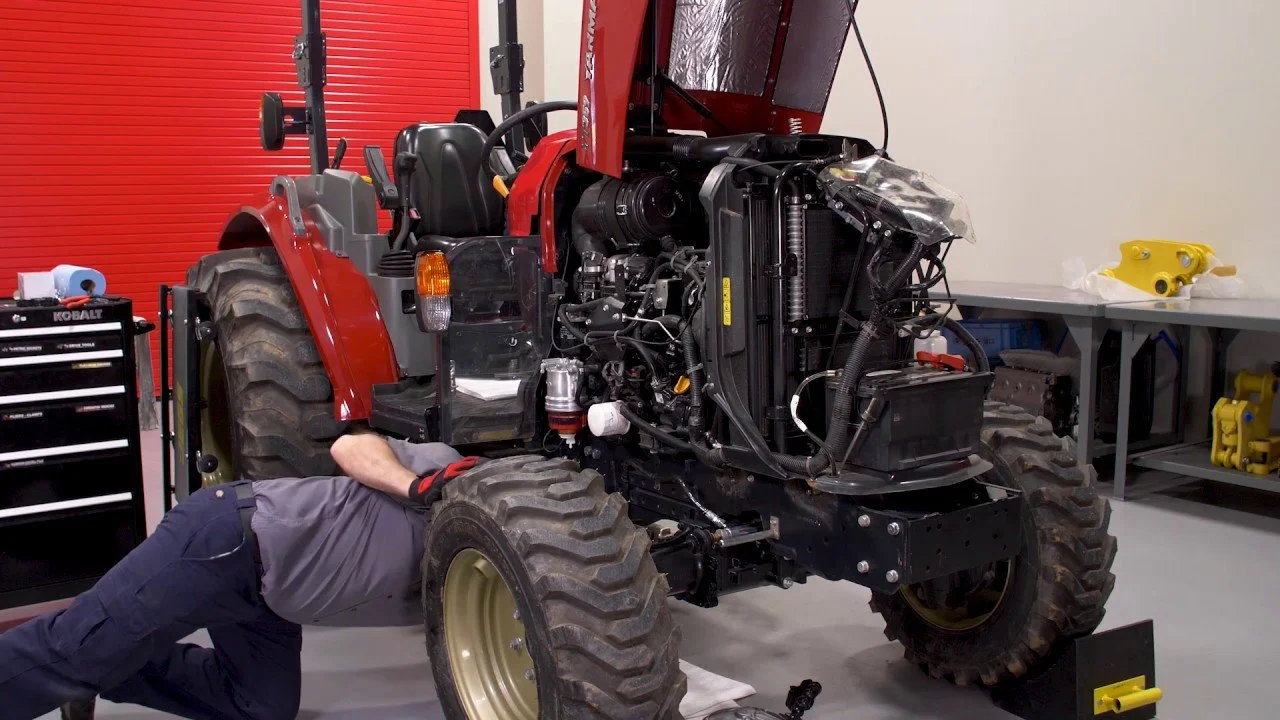 Person som arbetar under en Yanmar traktor i ett verkstadshus.