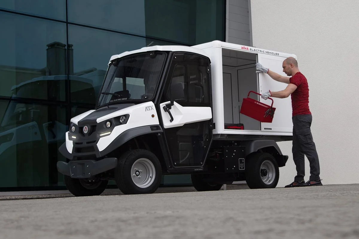 En man flyttar en röd verktygslåda in i en liten vit elektrisk Alkè utomhus.