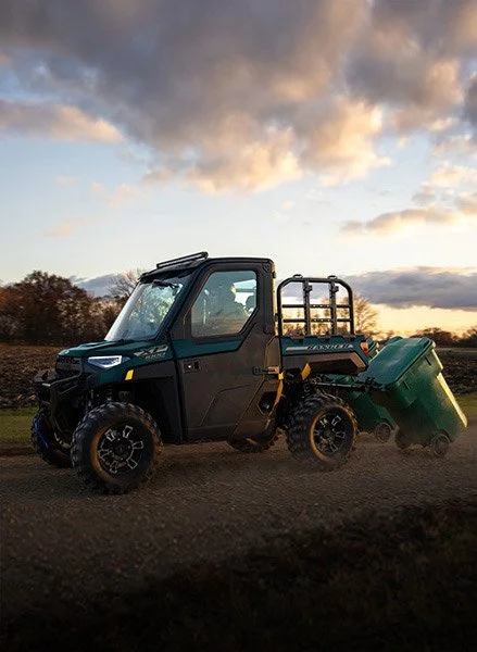 Polaris Ranger med en bakre container, åker på en landsväg under en molnig himmel vid solnedgången.