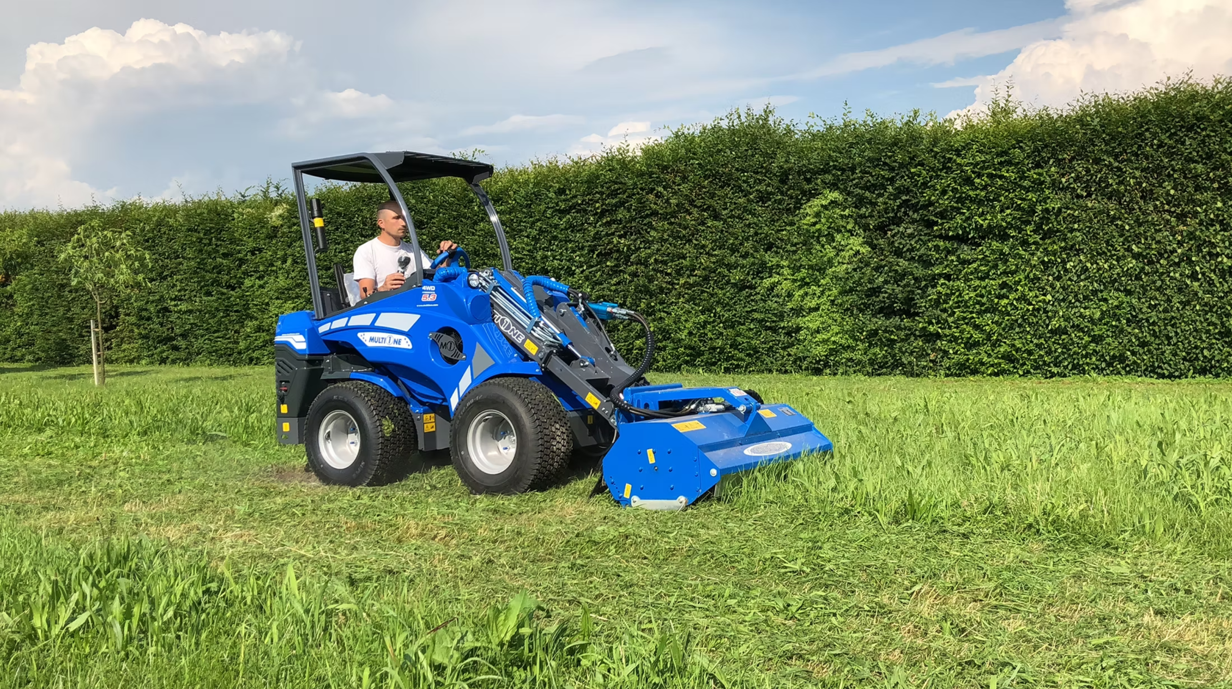 En man kör en MultiOne  med gräsklippare på en grön äng.