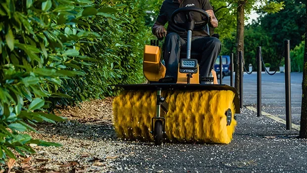 En person som kör en Stiga Park på en trottoar vid en grön buske.