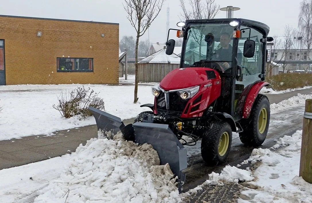 En röd Yanmar traktor med snöslunga som rensar snö på en trottoar.