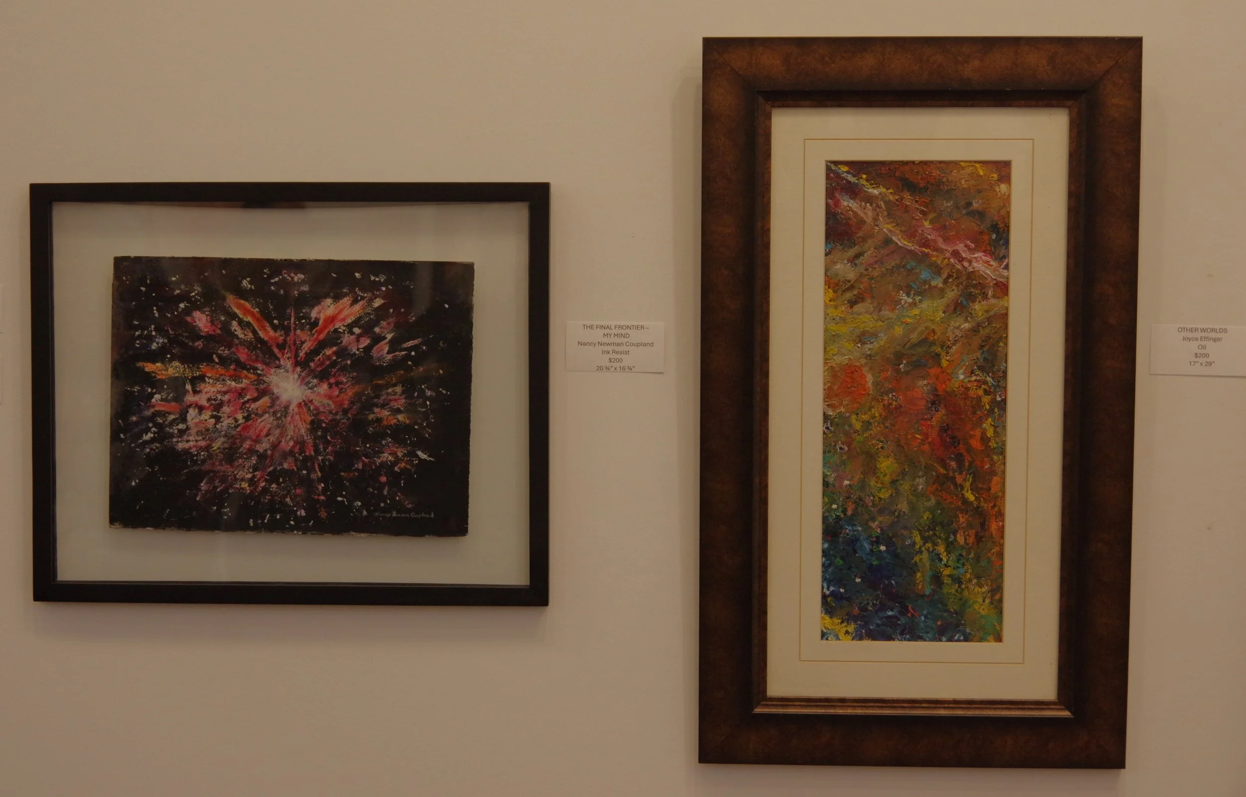 Two abstract paintings are displayed on a gallery wall. The left painting resembles a burst of red, pink, and white colors against a dark background. The right painting features a vertical, colorful, textured abstract design with a brown frame.
