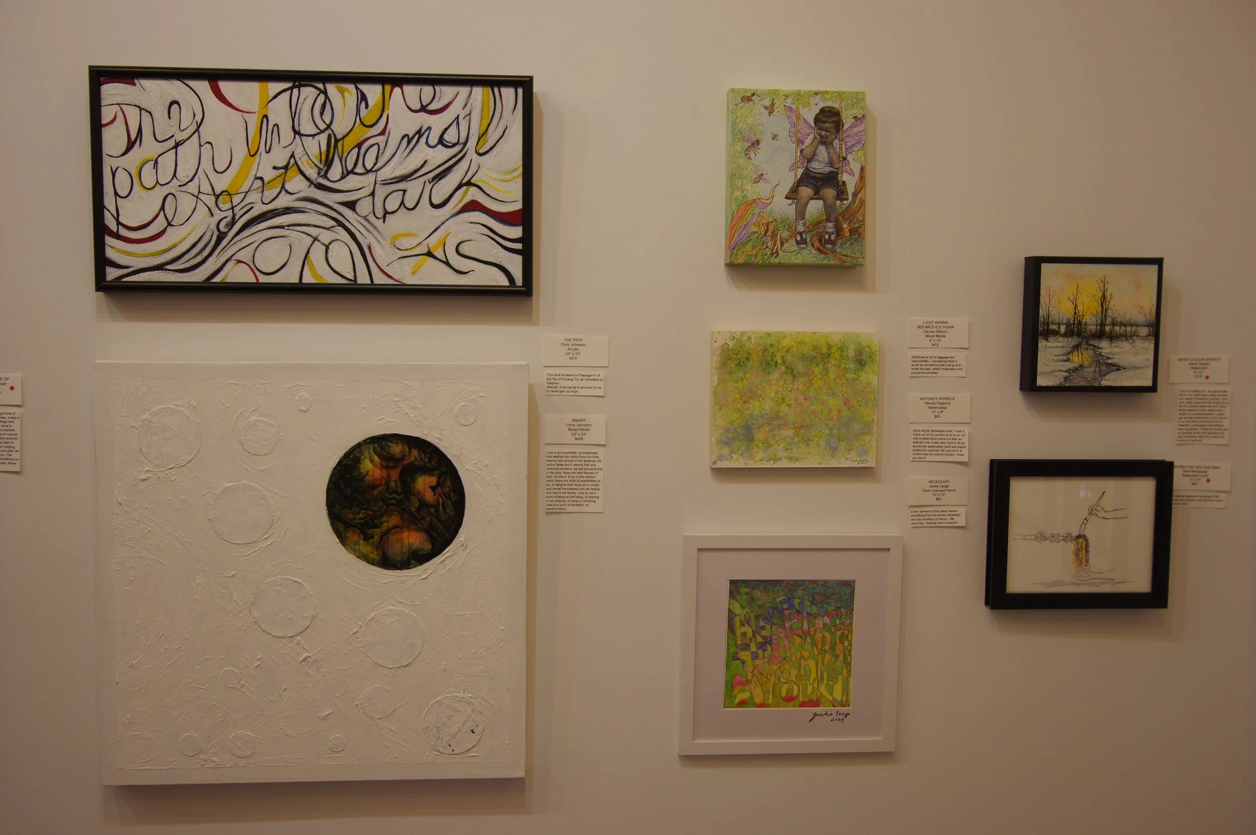 A wall of art gallery with multiple paintings and mixed media artworks, including abstract, landscape, figurative, and textured pieces.