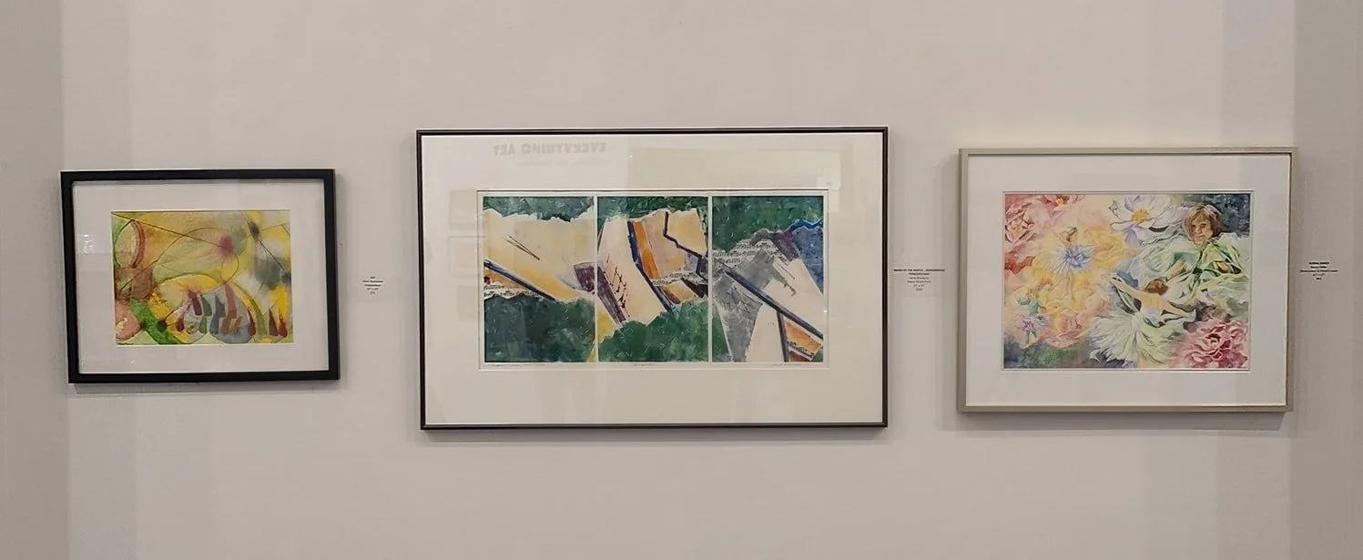 Three framed artworks hung on a white gallery wall, with the central piece being a triptych and the other two artworks being smaller.