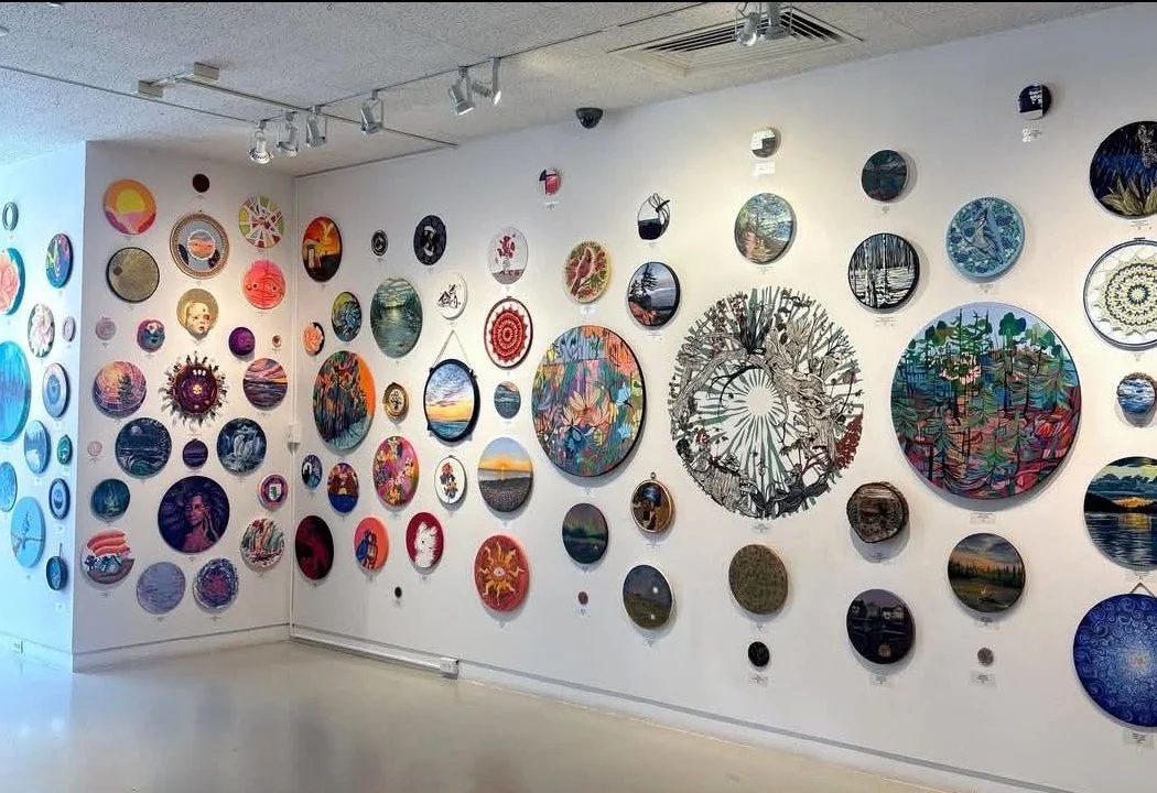 Art gallery wall with various circular paintings and mixed media artworks in different sizes and vibrant colors.