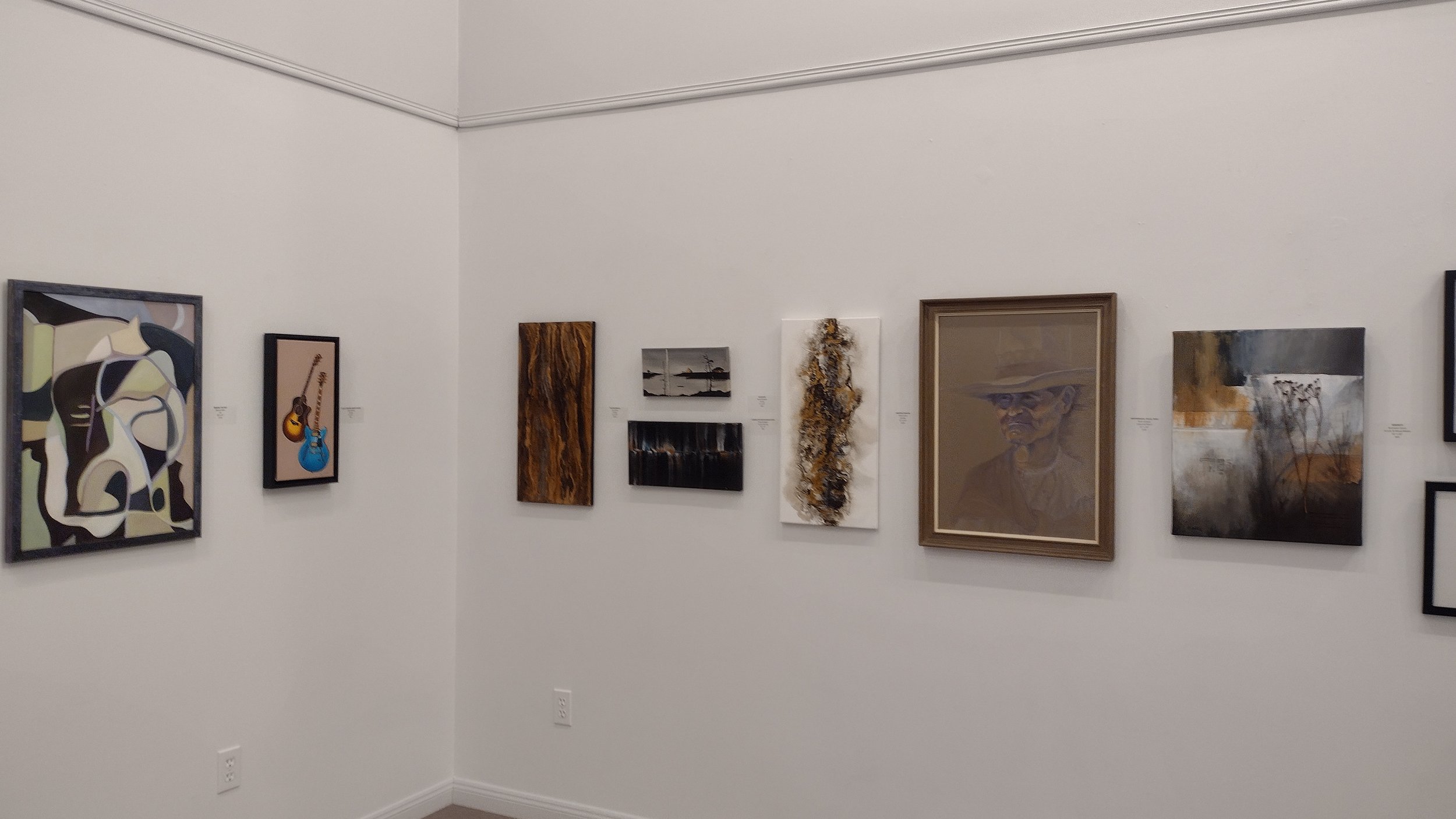 Wall in an art gallery with multiple paintings and artworks displayed.