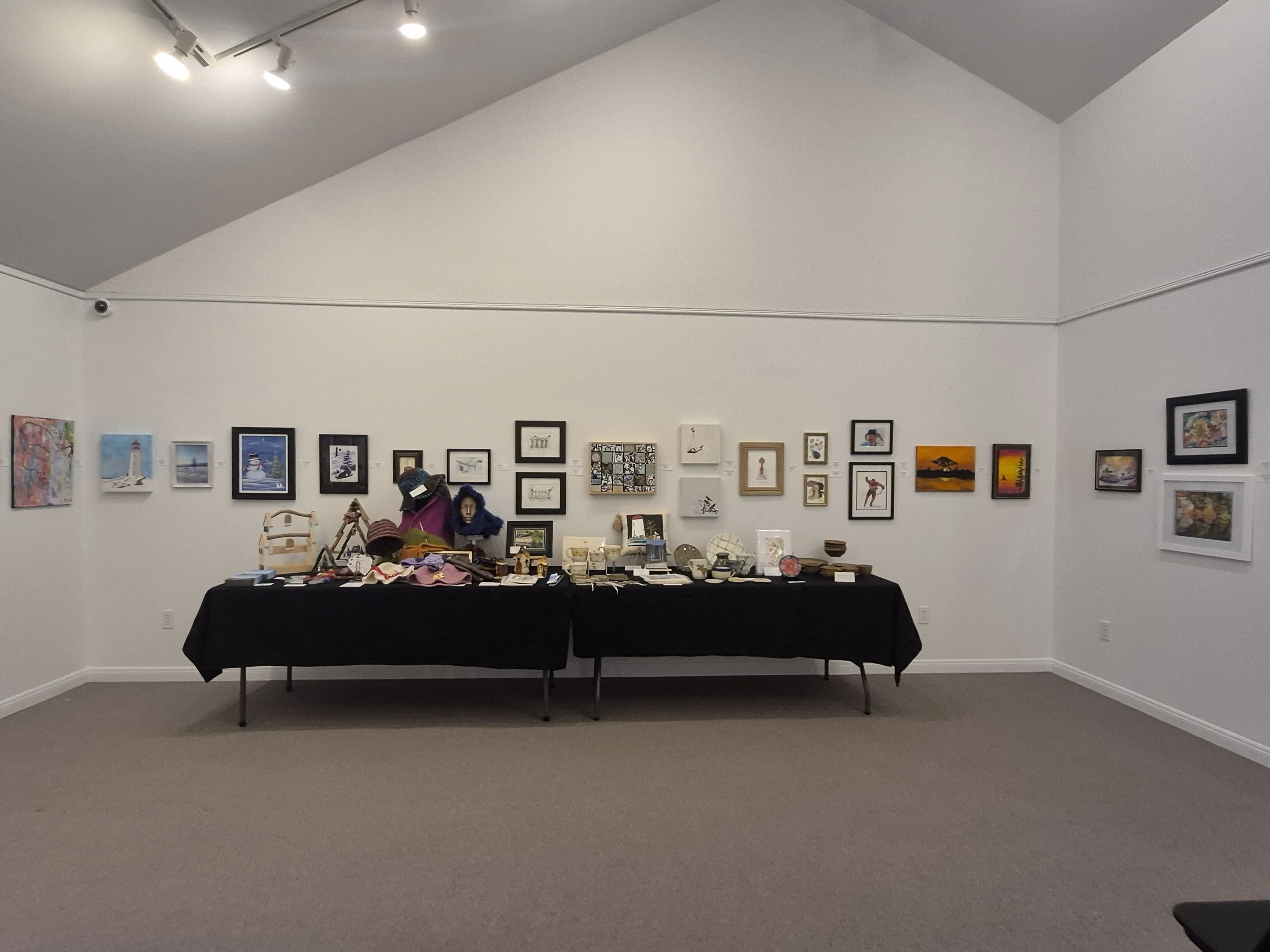 An art gallery with framed artwork on the walls and a table displaying various decorative items and crafts.