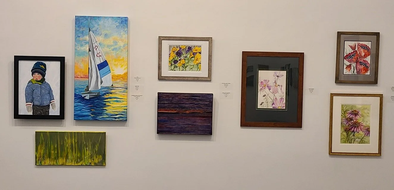 Gallery wall with nine paintings of various subjects, including a child in winter clothing, a sailboat on the water at sunset, wildflowers, an abstract landscape, and floral art.