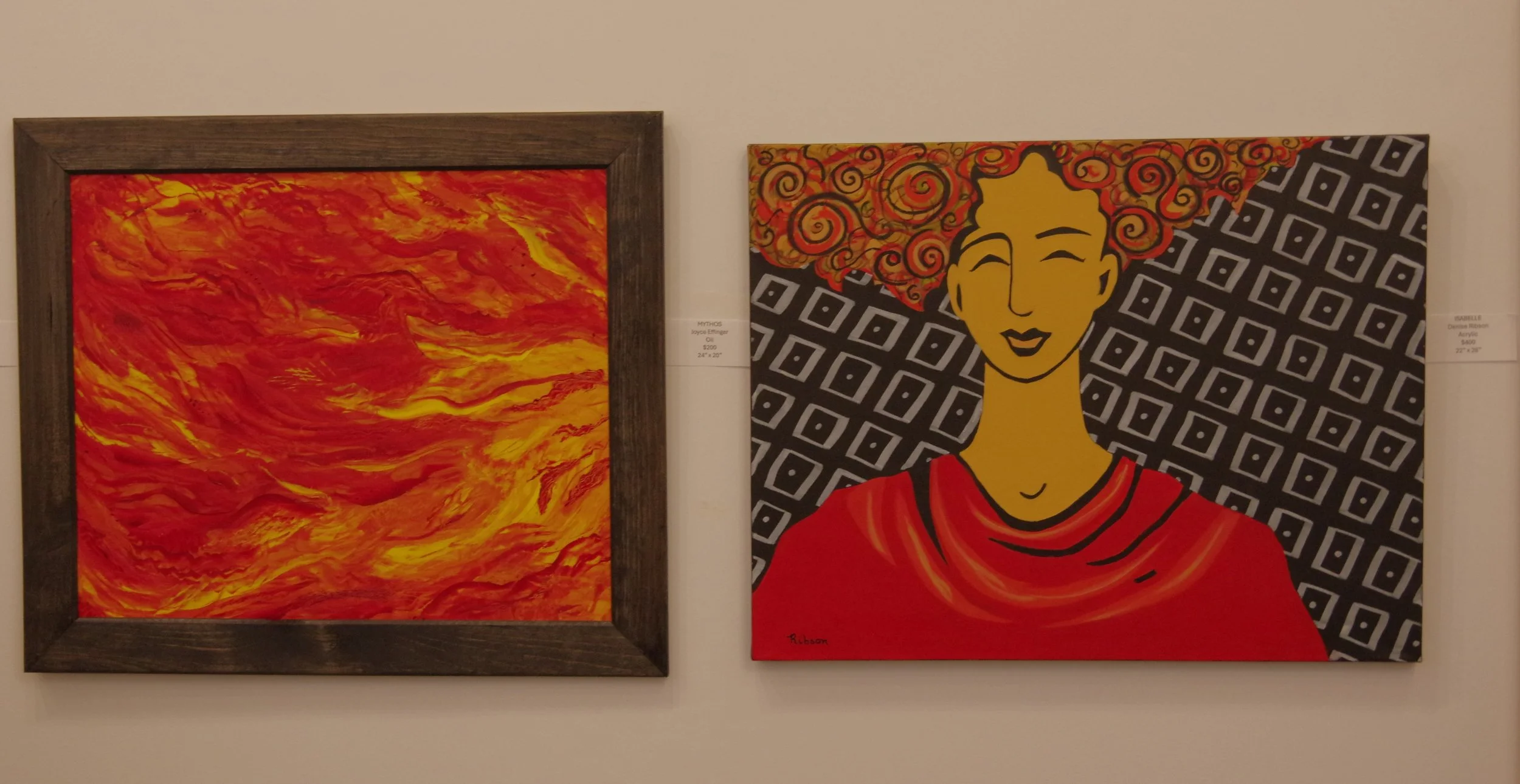 Two paintings hanging on a white gallery wall. The left painting features an abstract swirl of red and yellow colors. The right painting shows a stylized portrait of a woman with short curly red hair, bright yellow skin, a red top, and a patterned background of black and white geometric shapes.