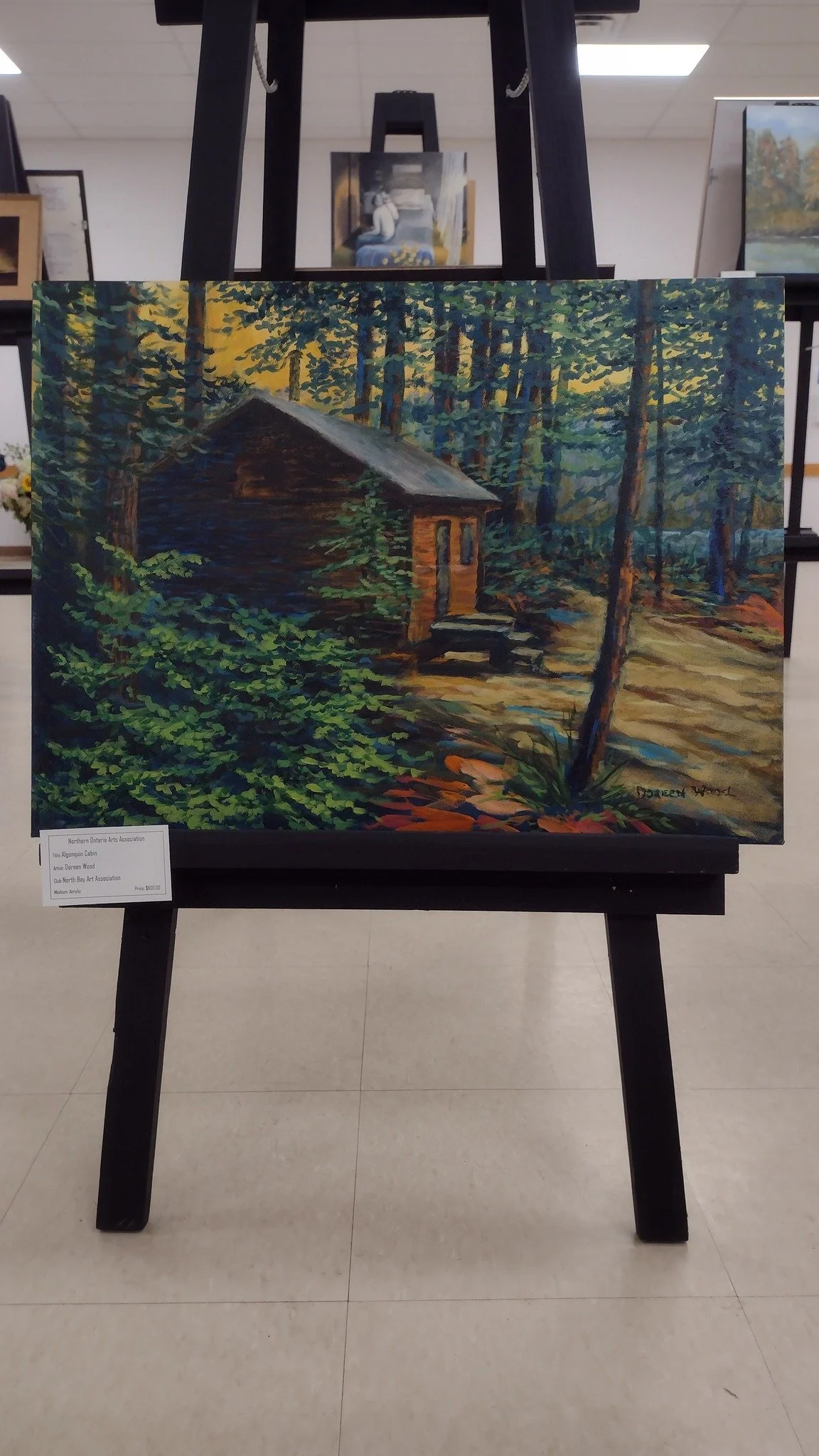 A painting of a wooden cabin in a forest, with trees and foliage surrounding it, painted in vibrant colors.