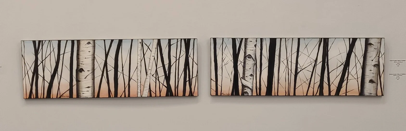 Two horizontal paintings of a forest of white birch trees with a pastel sunset sky in the background, mounted on a white wall.