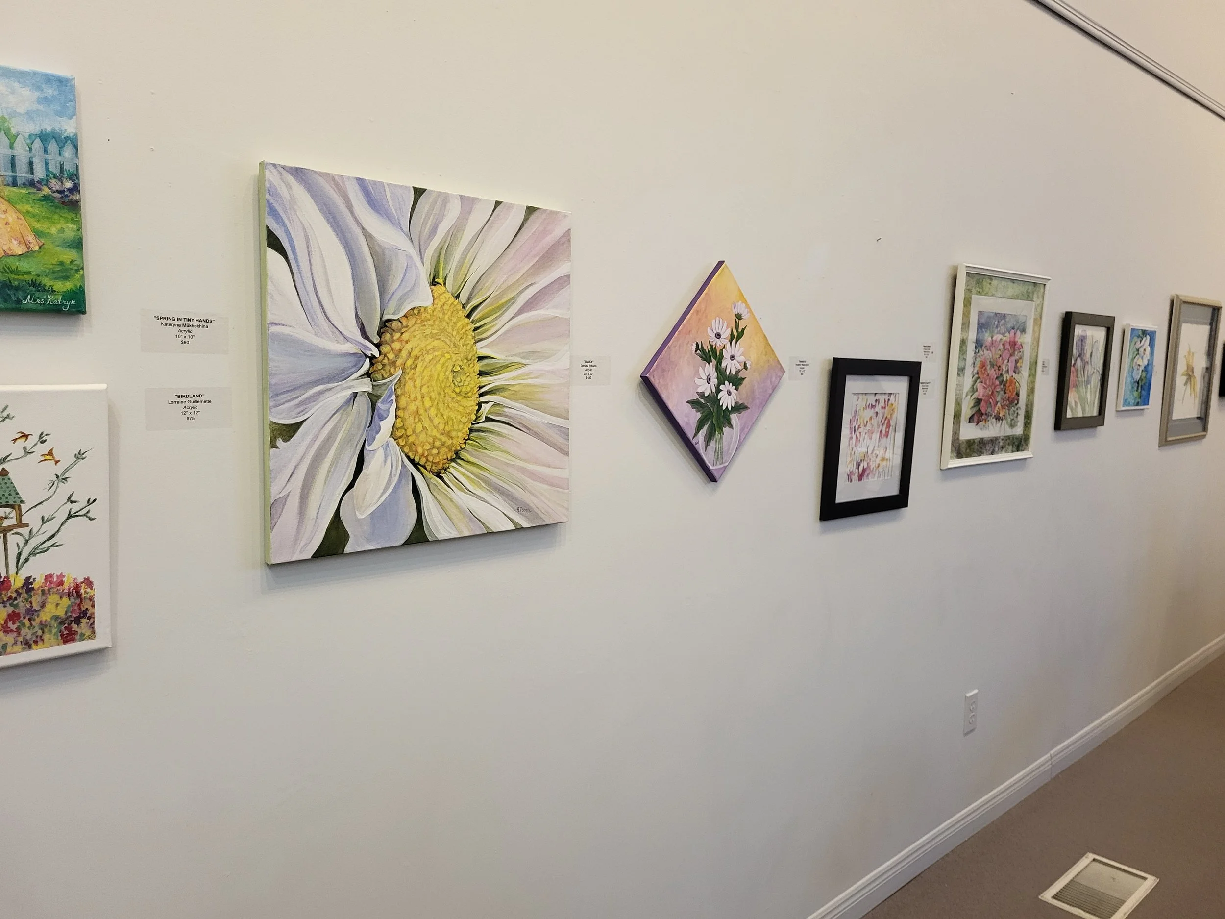 Gallery wall featuring various colorful paintings of flowers and flowers on paper, some framed and some on canvas.