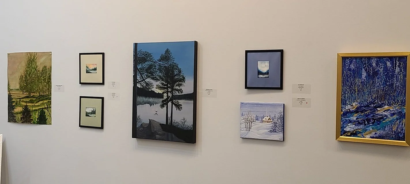 A gallery wall displaying eight landscape paintings of different sizes and styles, including nature scenes like trees, lakes, and snowy landscapes.