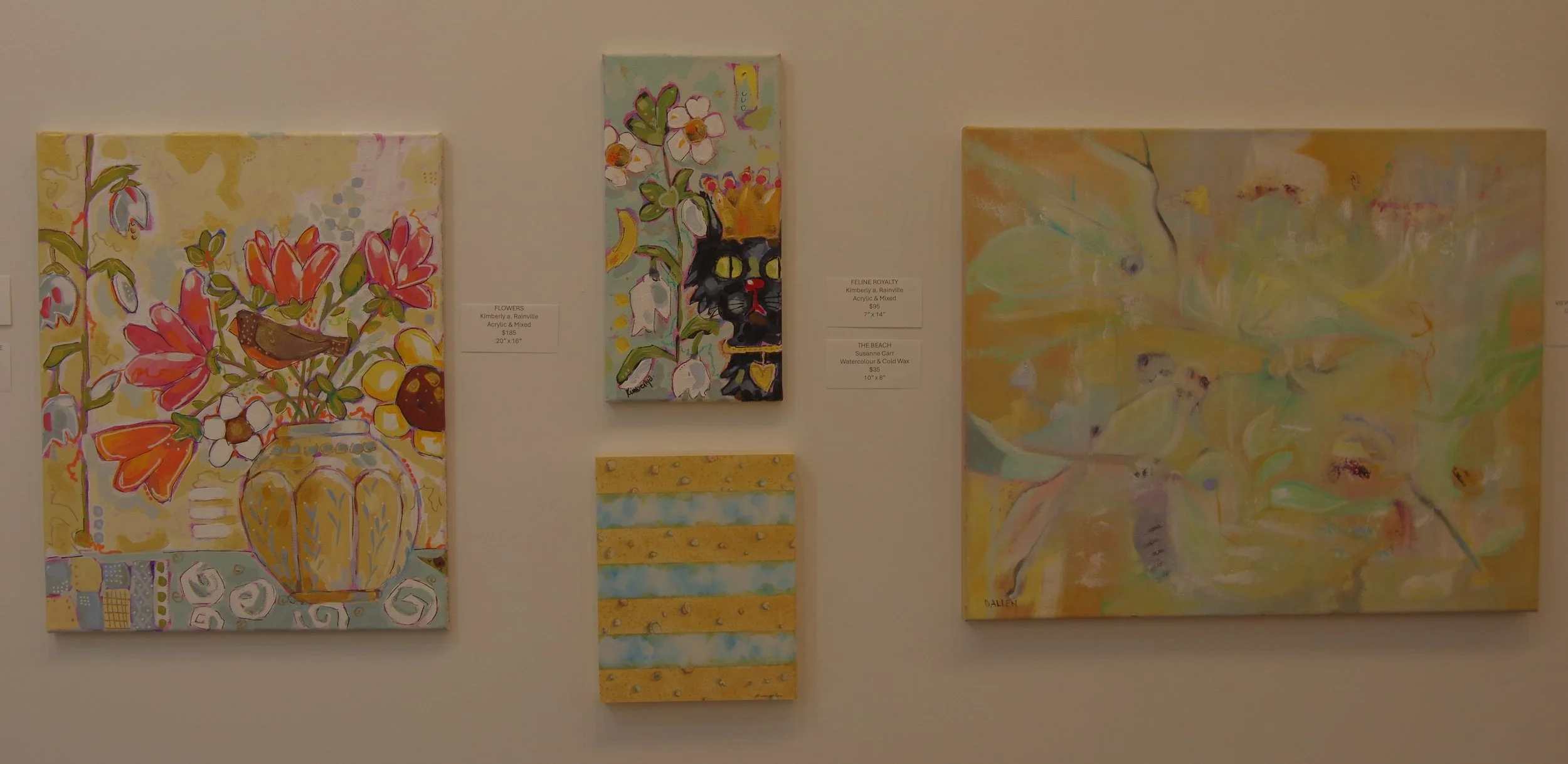 A gallery wall displaying four colorful paintings, including a floral still life with a vase, a cat portrait, an abstract piece with pastel colors, and a striped abstract pattern.