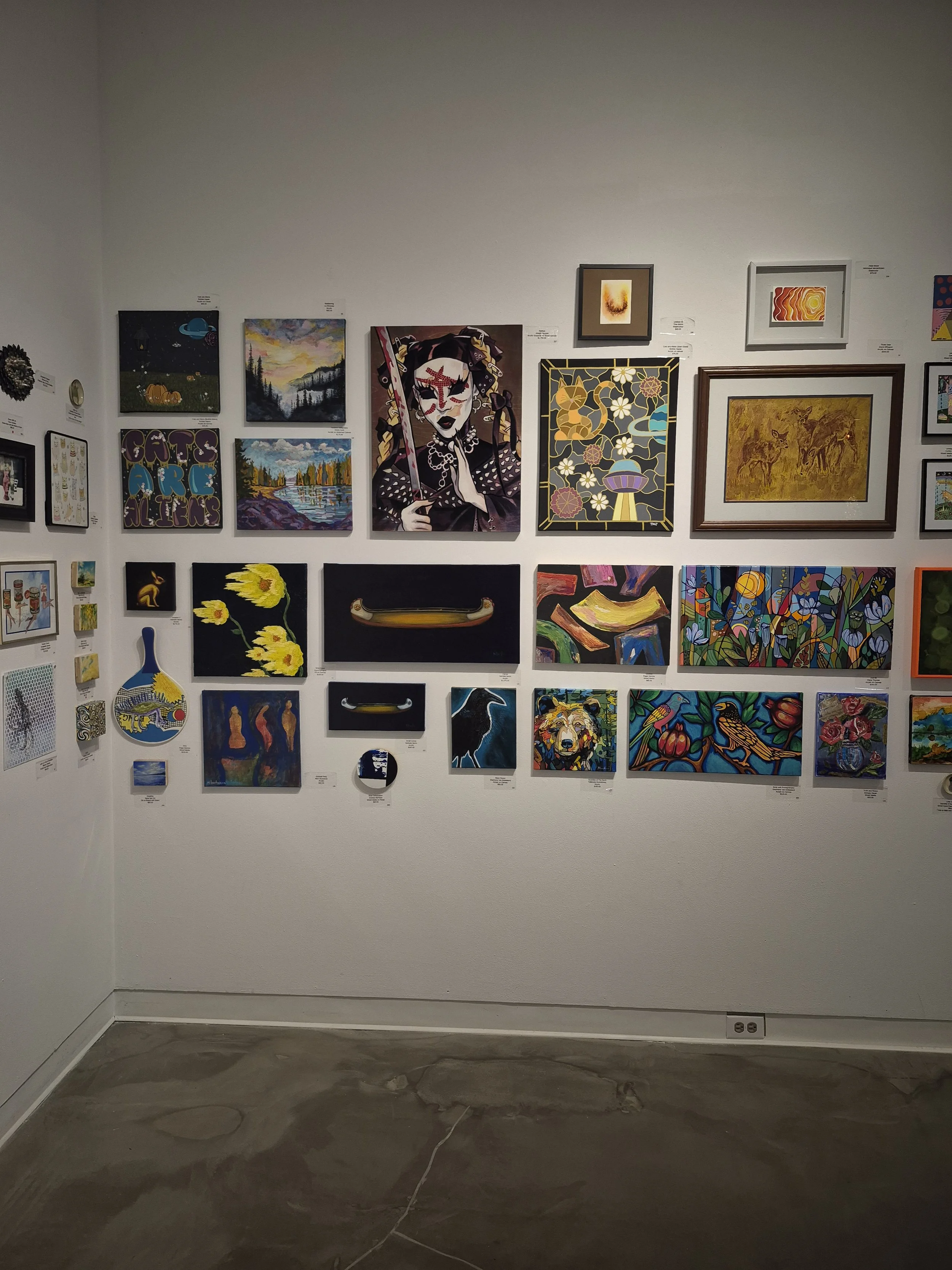 Gallery wall displaying various colorful paintings, portraits, landscapes, and abstract art.