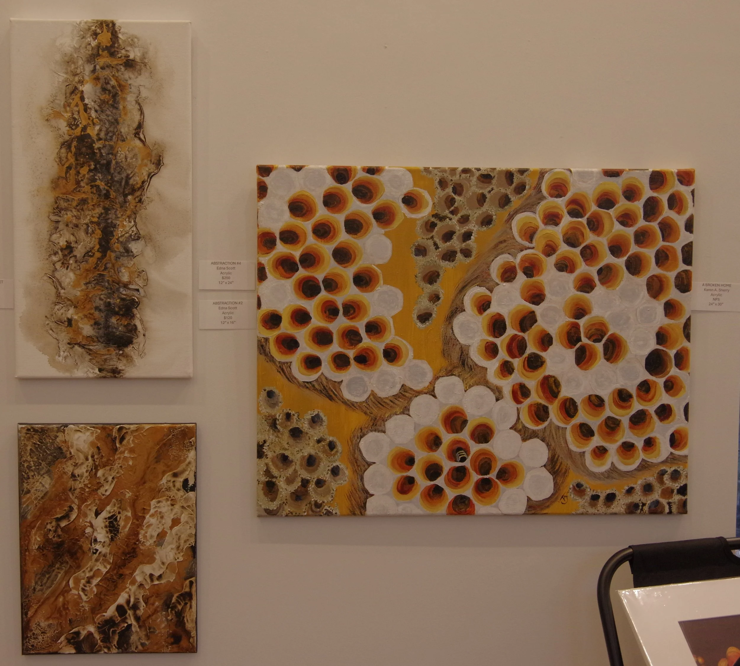Group of three abstract paintings, one large and two smaller, featuring earthy tones and organic patterns, on a gallery wall.