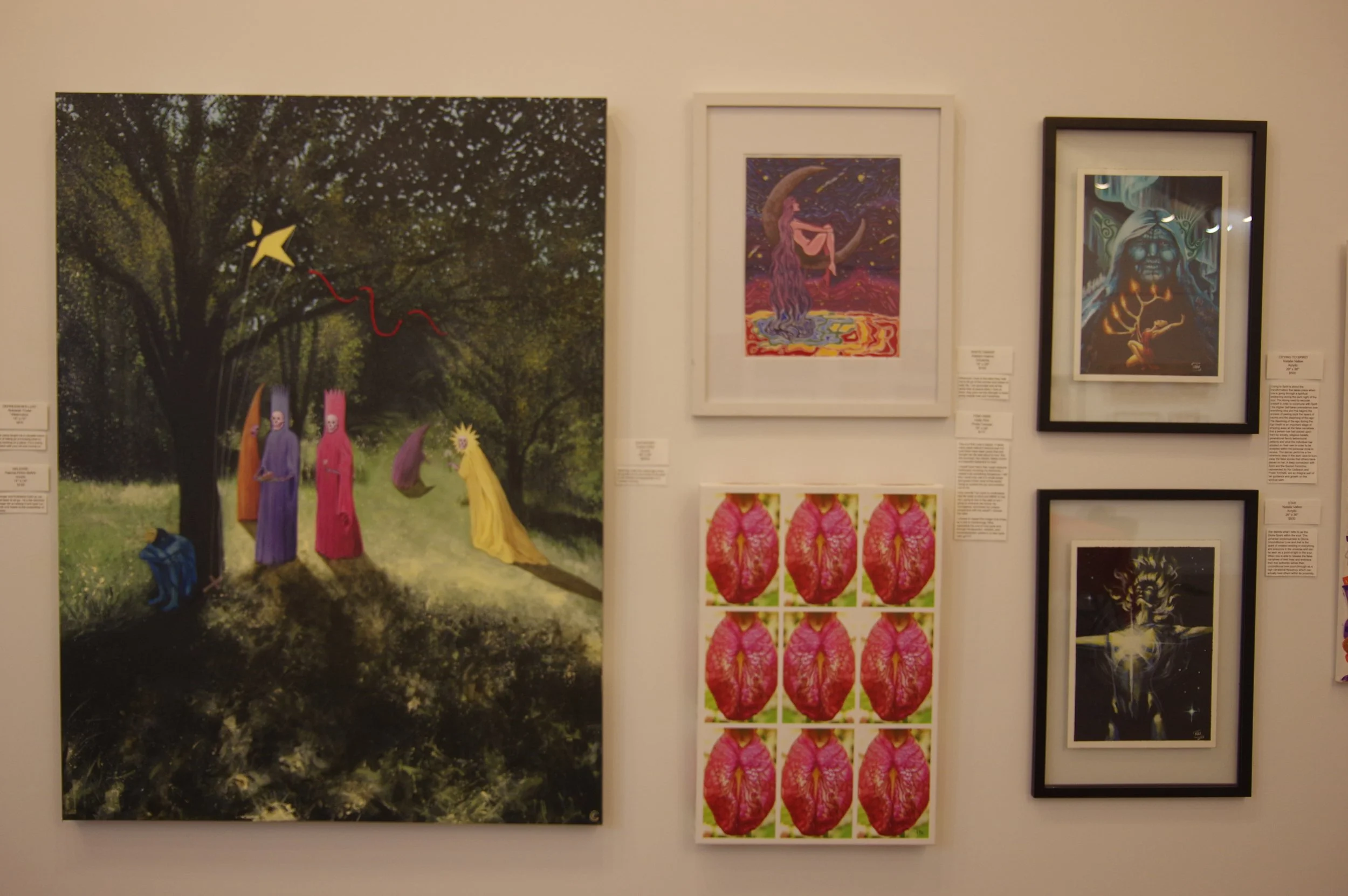 Gallery wall with five framed art pieces including a large surreal painting of figures with pink headgear under a tree, a colorful celestial scene with a figure on a crescent moon, a portrait with a glowing face in a dark environment, a series of nine pink and green symmetrical images, and an abstract light-filled figure.
