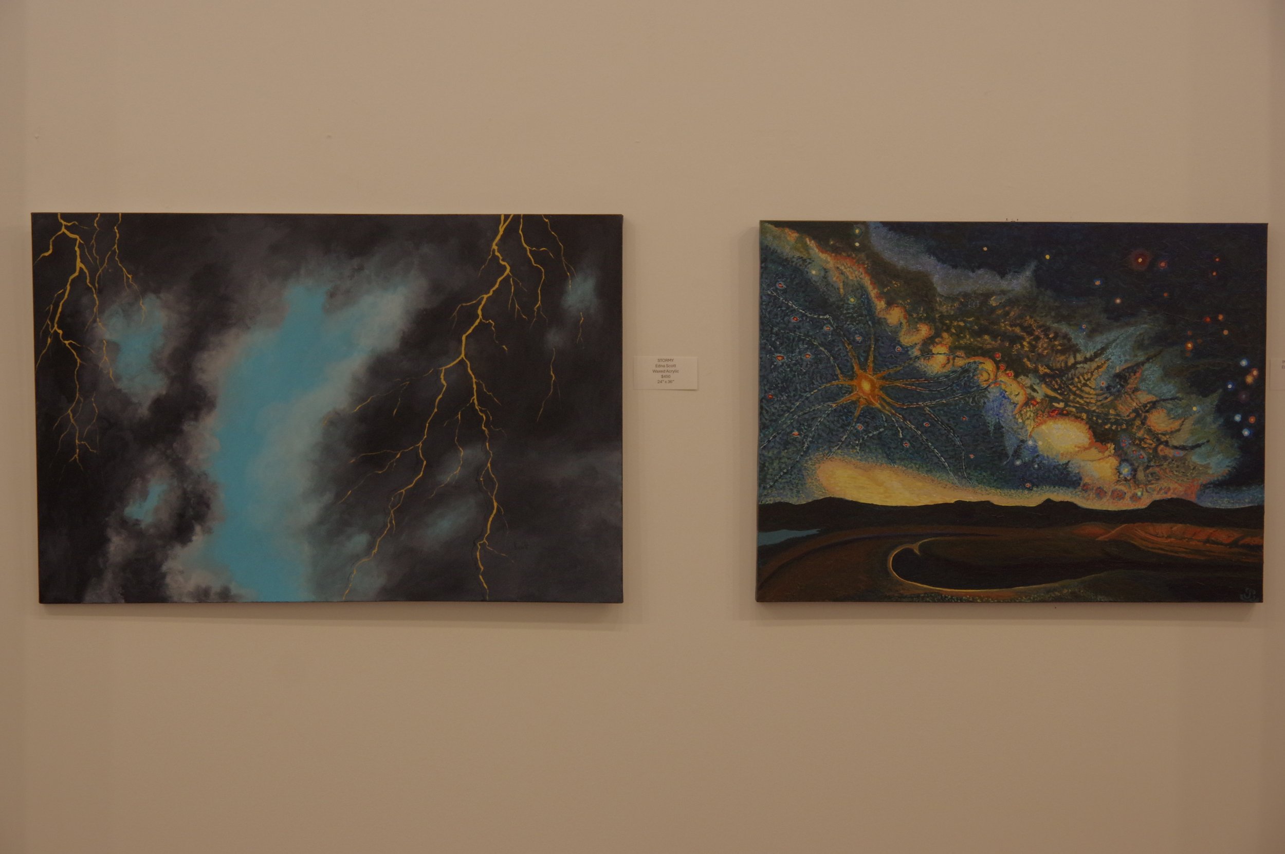 Two paintings on a wall, one depicting a storm with lightning and clouds, the other showing a cosmic scene with stars, planets, and nebulae.