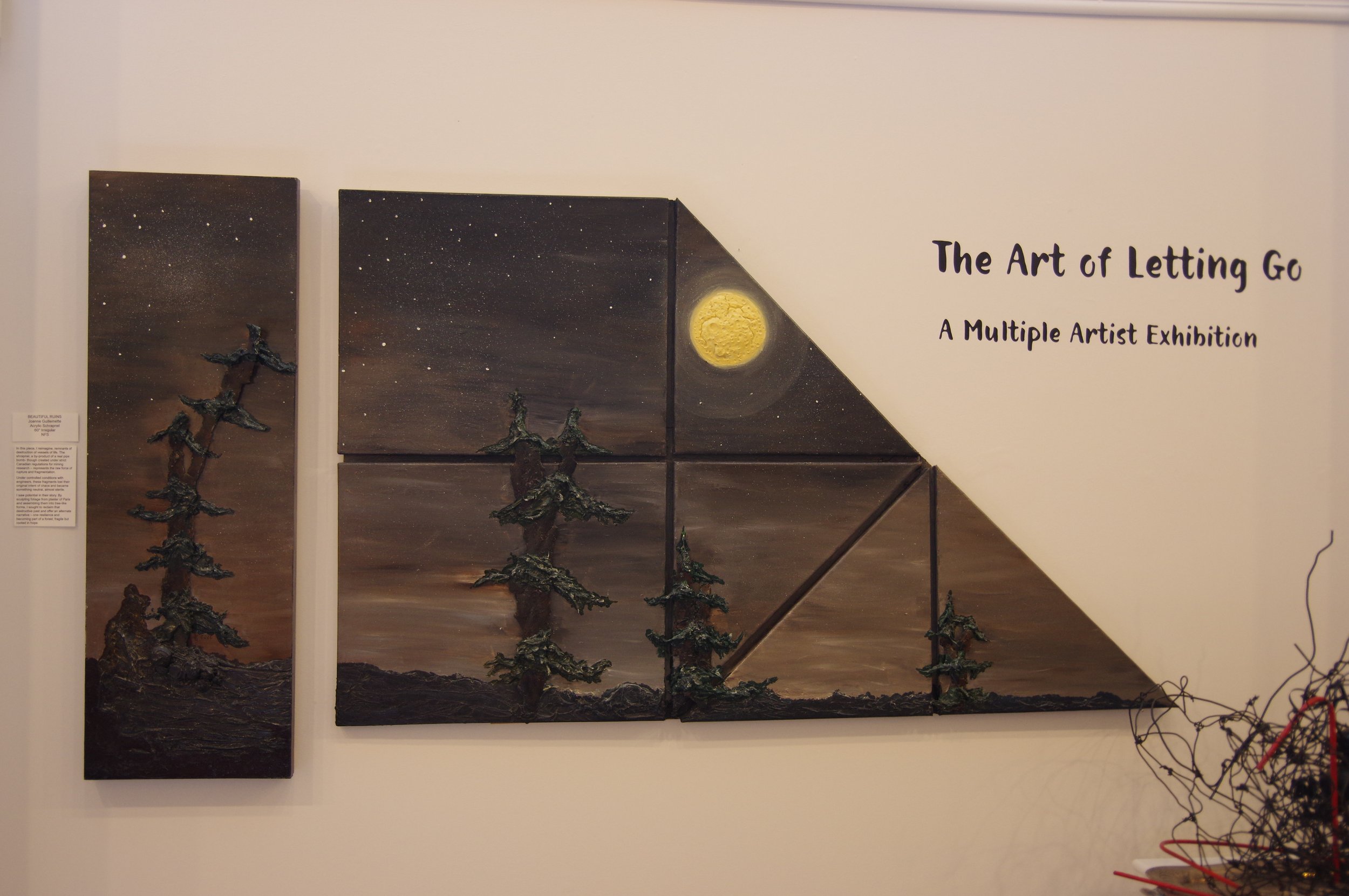 An art exhibit titled 'The Art of Letting Go' featuring a multi-panel painting of a nighttime landscape with a full moon, stars, and silhouetted pine trees.
