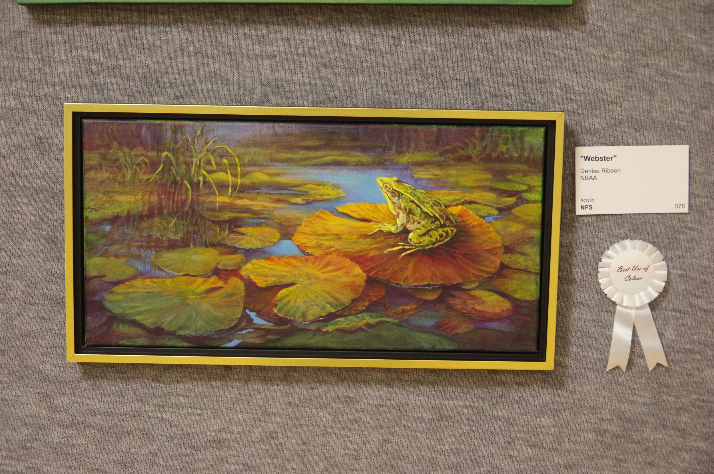 A painting titled 'Webster' by Denise Ribson, featuring a frog sitting on a large lily pad in a pond with numerous lily pads and water plants. The scene has vibrant green, yellow, and brown hues, with reflections in the water.