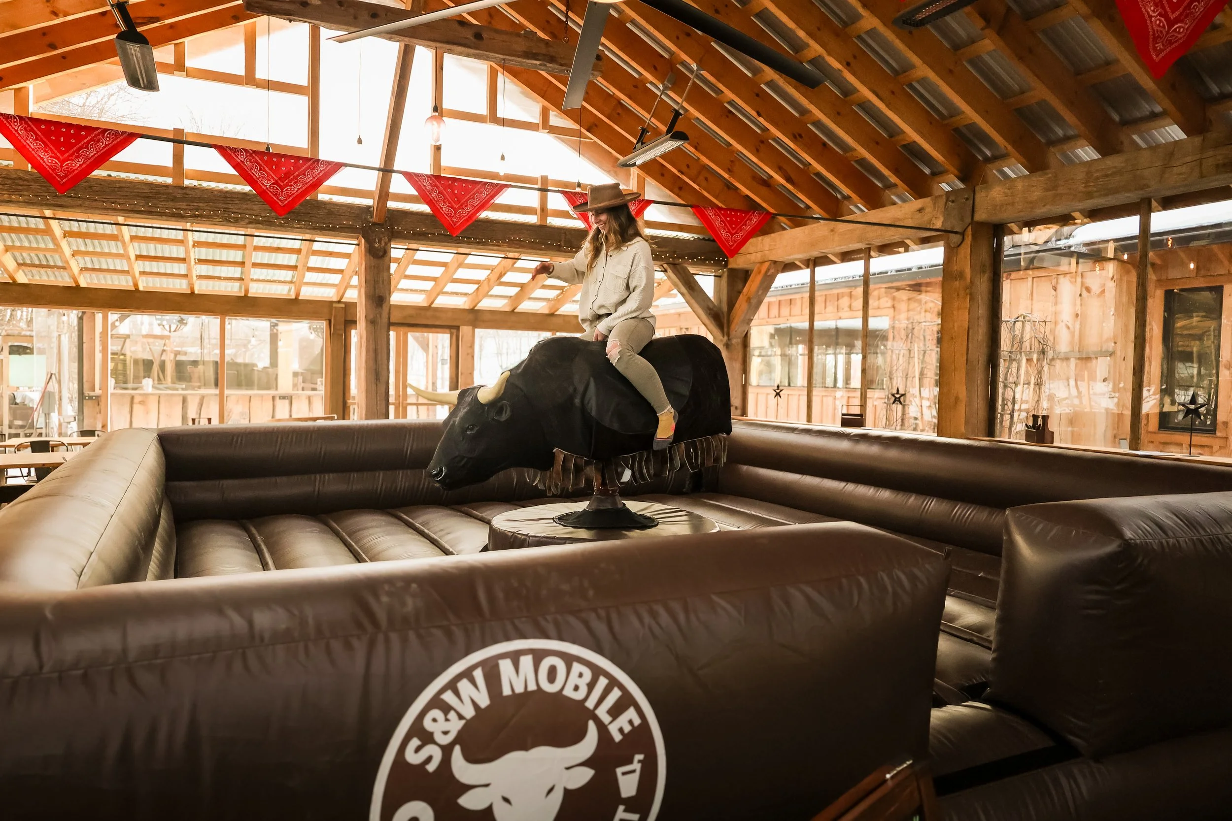 A woman wearing a cowboy hat riding S&W Mobile Entertainment's mechanical bull at a brewery in Ulster Park New York