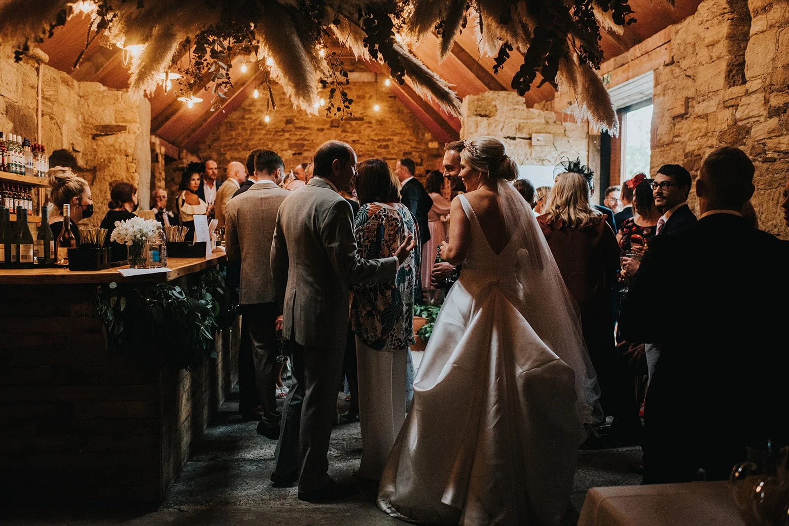 People at a wedding reception in a rustic venue with exposed brick walls and soft lighting, mingling and celebrating.