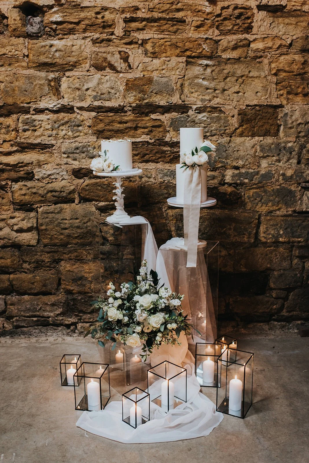 Wedding candles, flowers, and lanterns arranged against an exposed brick wall.
