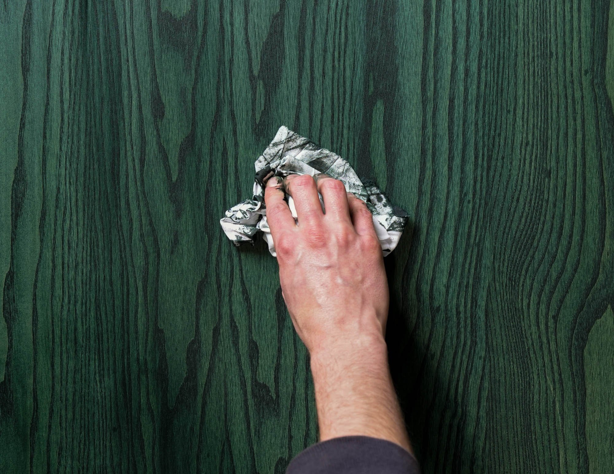 A person's hand wiping a green wooden surface with a cloth.