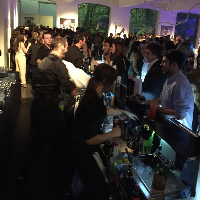 Crowded indoor bar at a social event with people talking and drinking.