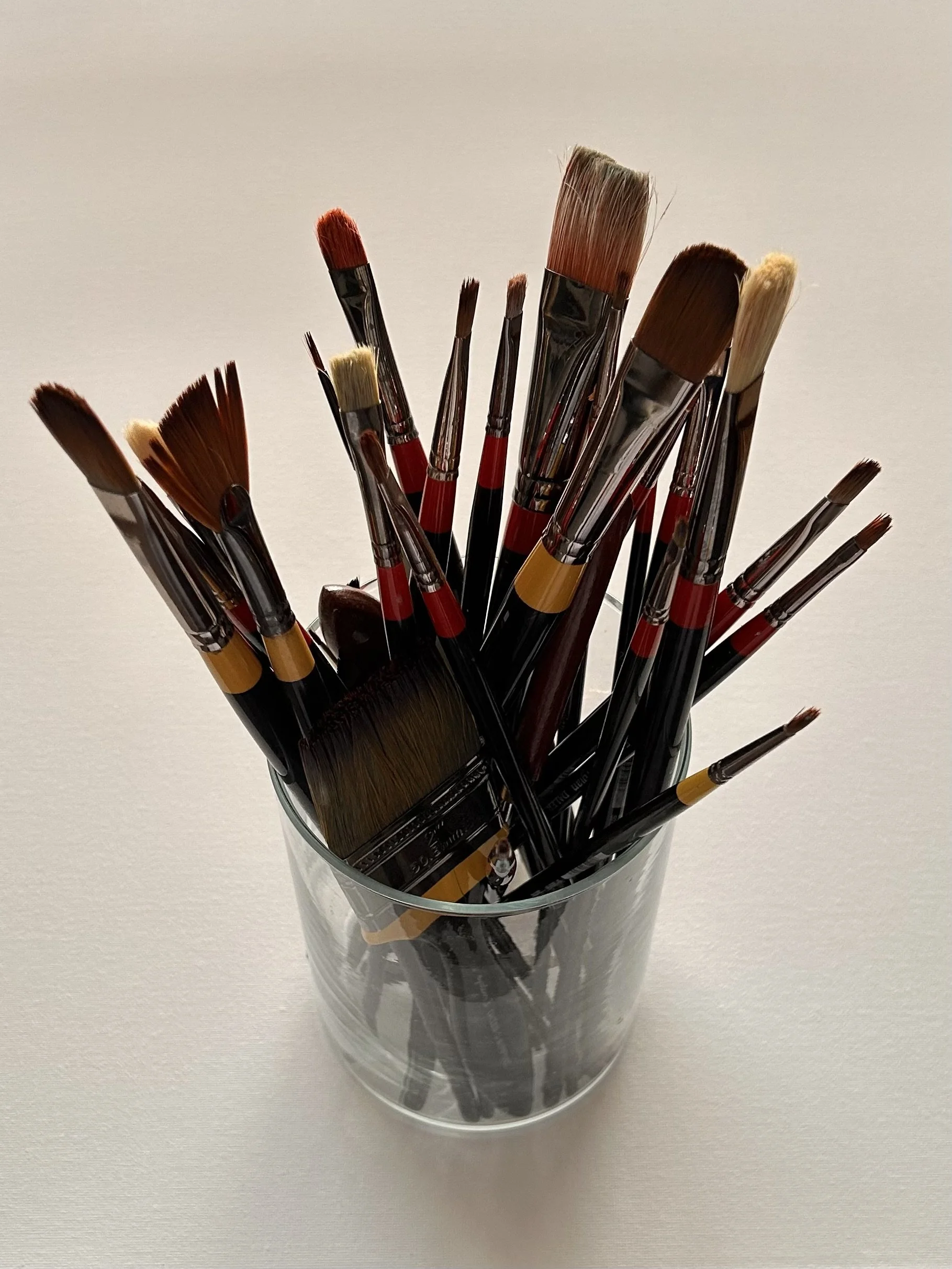 A glass container holding various paintbrushes with different sizes and shapes.