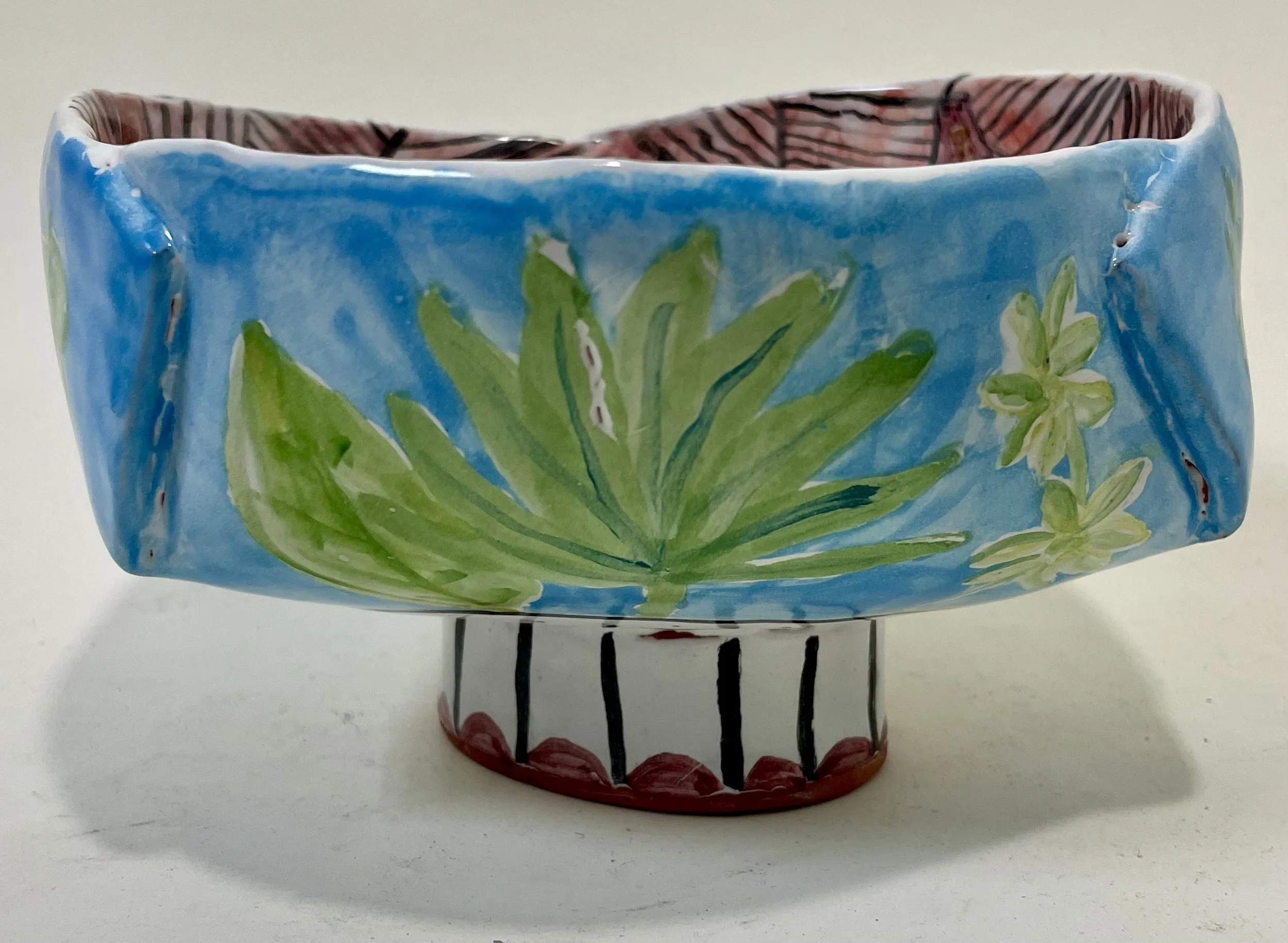Handmade ceramic bowl painted in blue, green, white, and red and decorated with leaf and flower patterns.