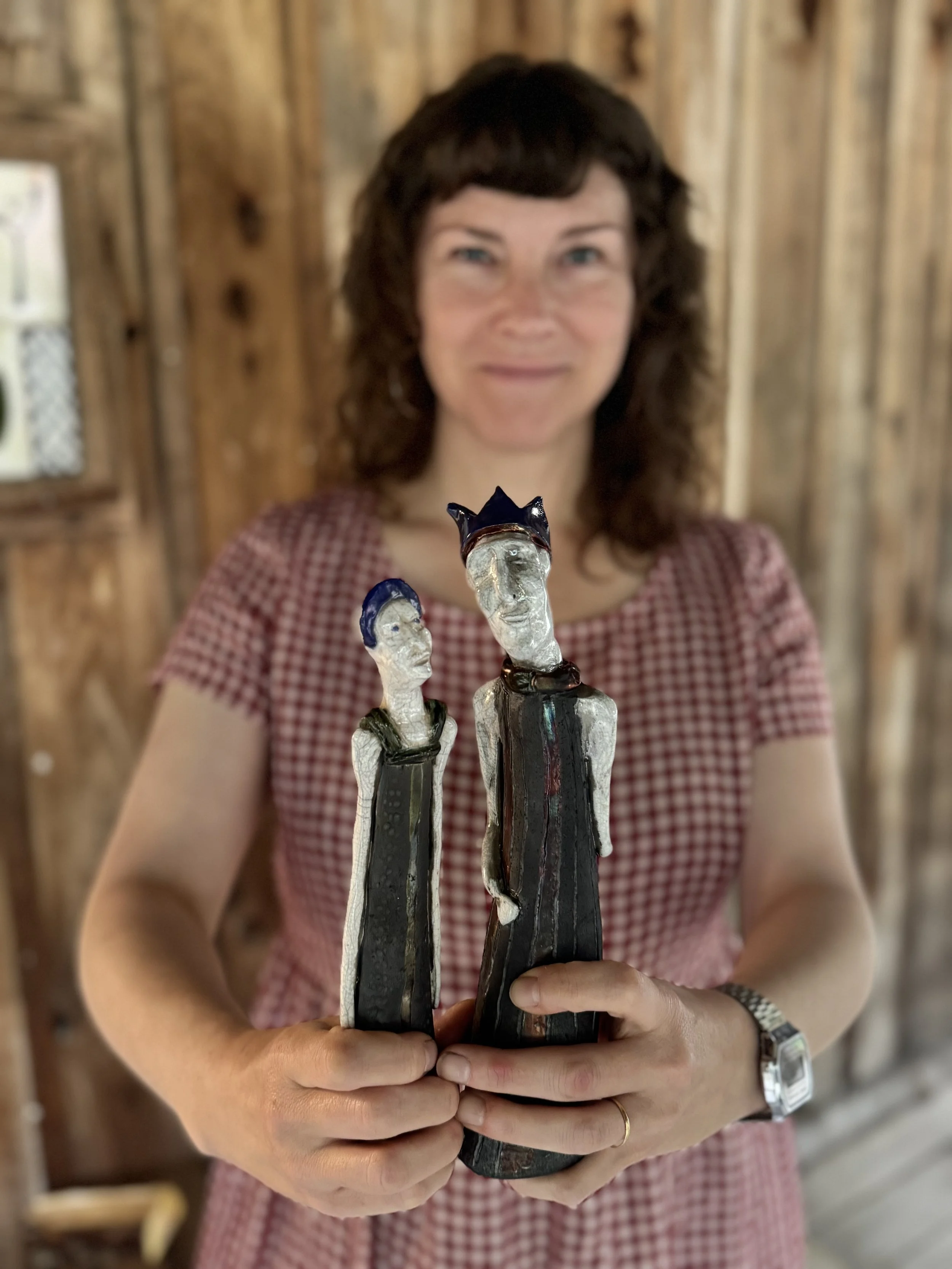 Yasmine Kiss holding two ceramic figurines of people with elongated bodies, one wearing a crown.