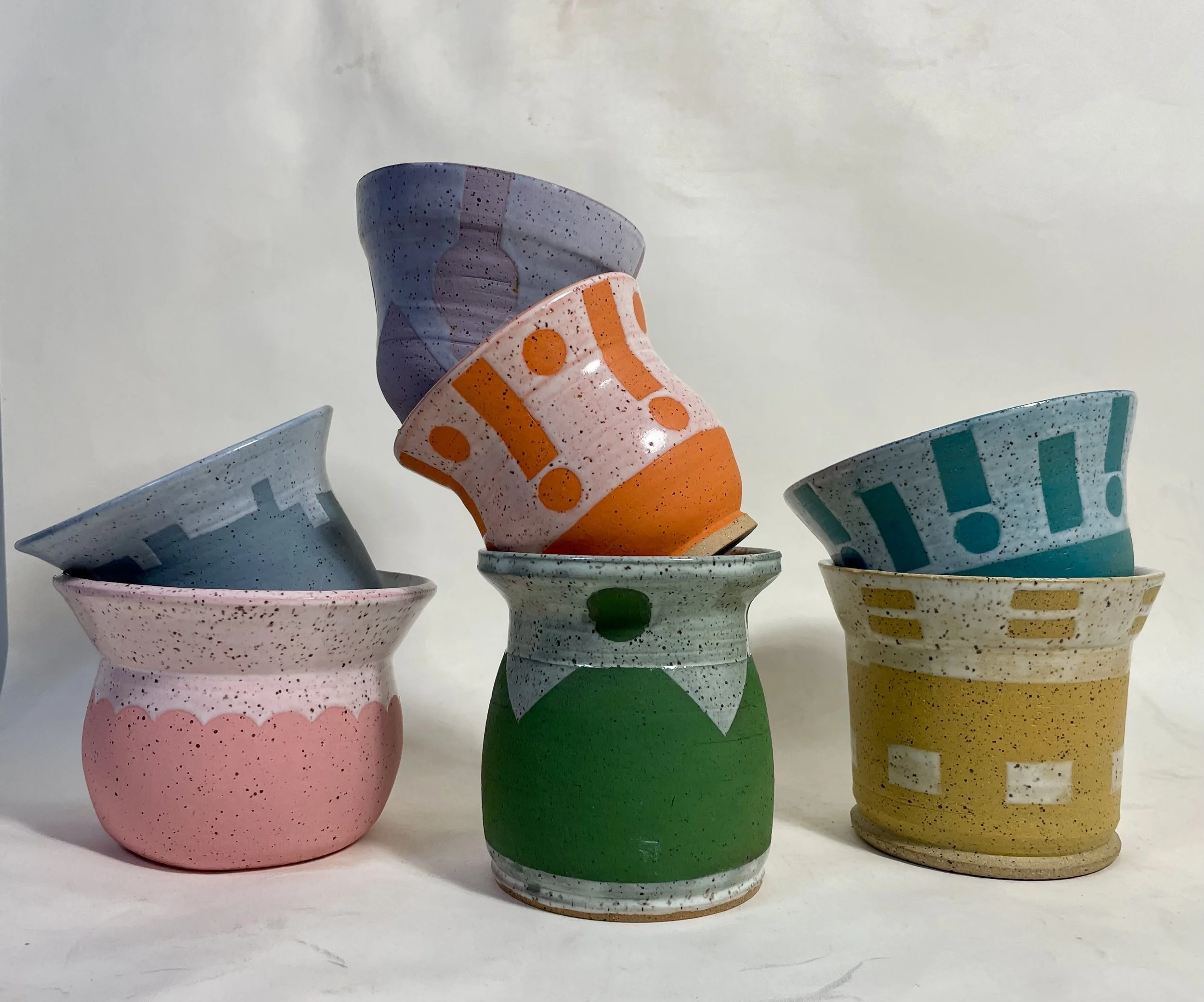 Colorful ceramic cups with abstract and geometric patterns arranged in a pyramid-like structure on a white background.
