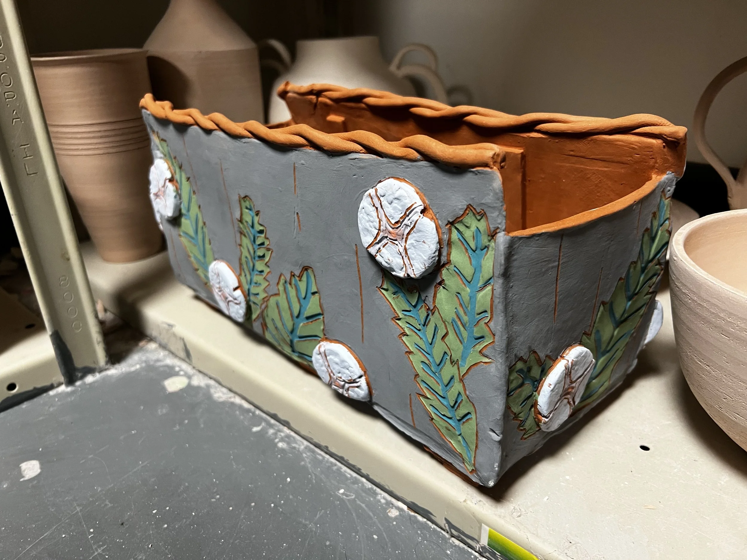 Handmade ceramic planter box decorated with leaves and cotton boll designs, with a braided rim.