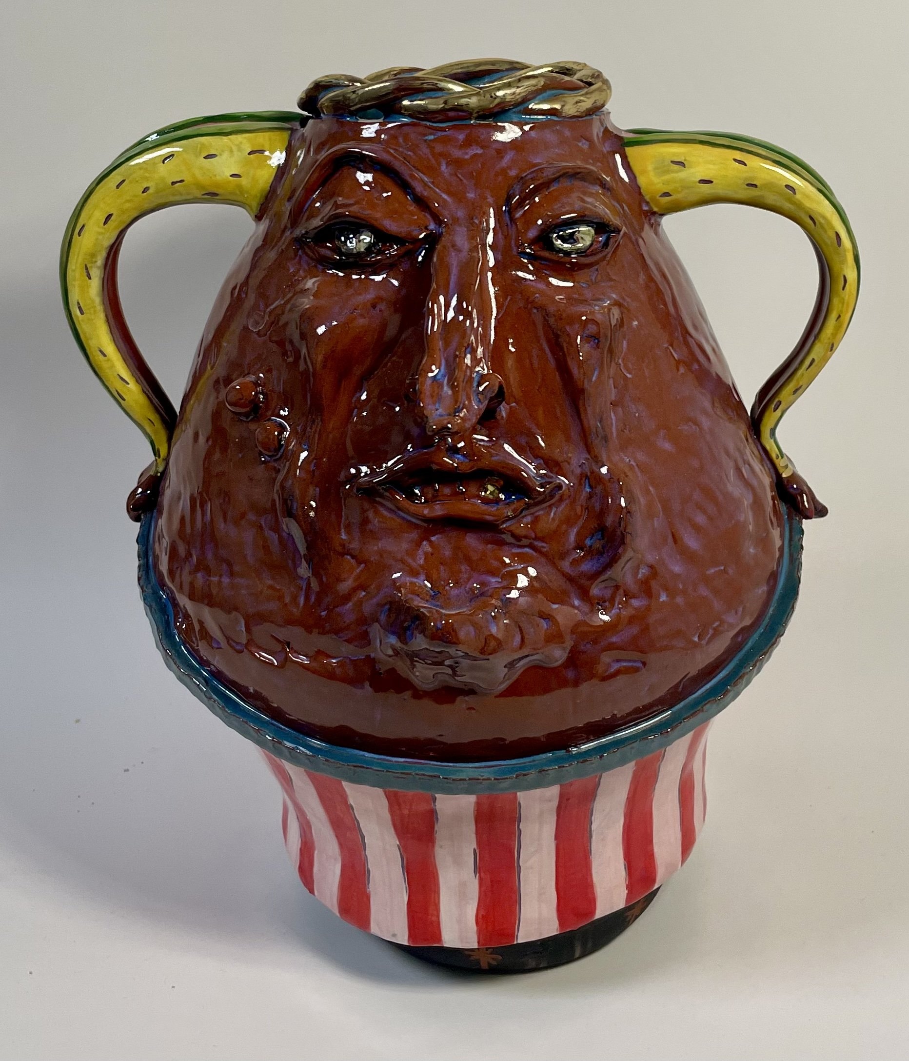 Colorful two-handled ceramic vase with a face, featuring detailed facial features and a red and white striped base.