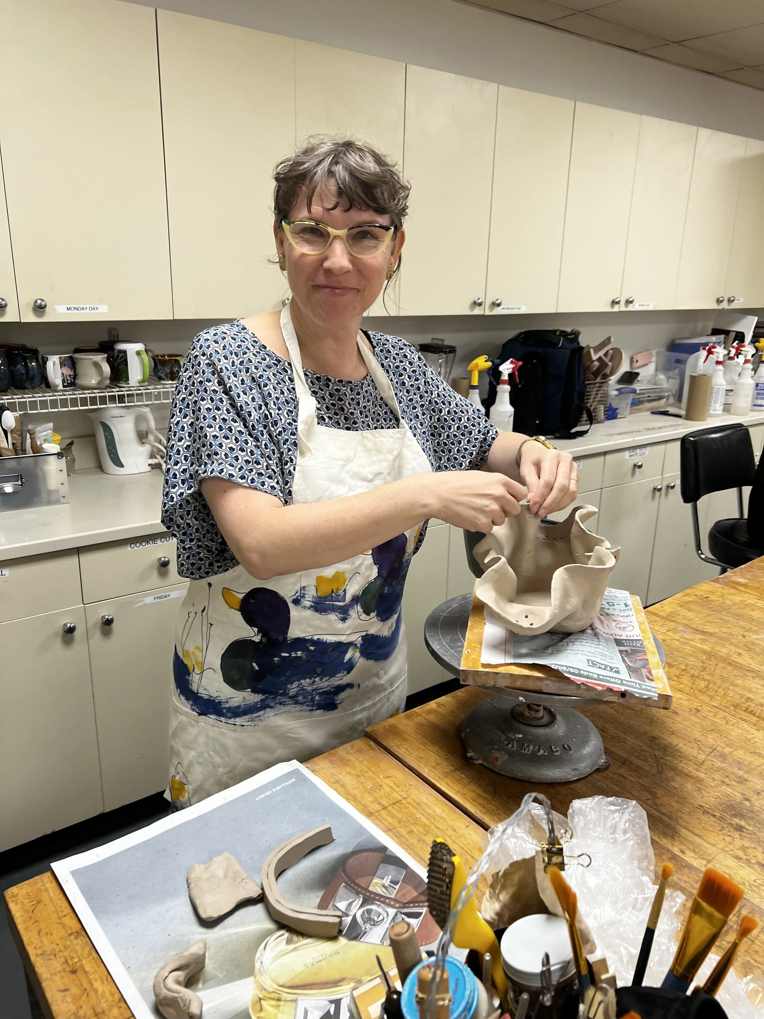Yasmine Kiss in glasses and an apron working on a clay sculpture in a pottery studio.