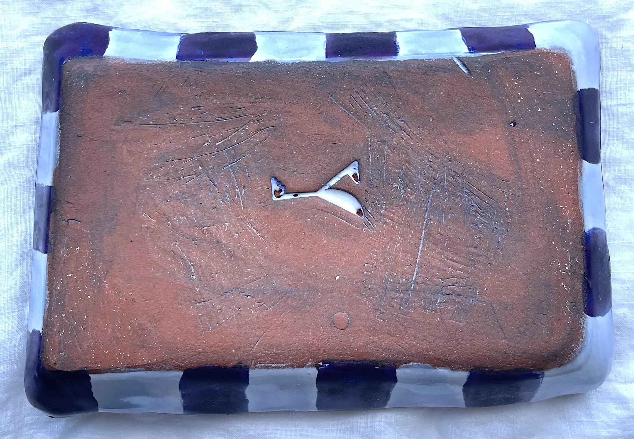 The underside of a rectangular ceramic tray with a black-and-white border. Inside the unglazed bottom of the tray is a chop with the initials "YK."