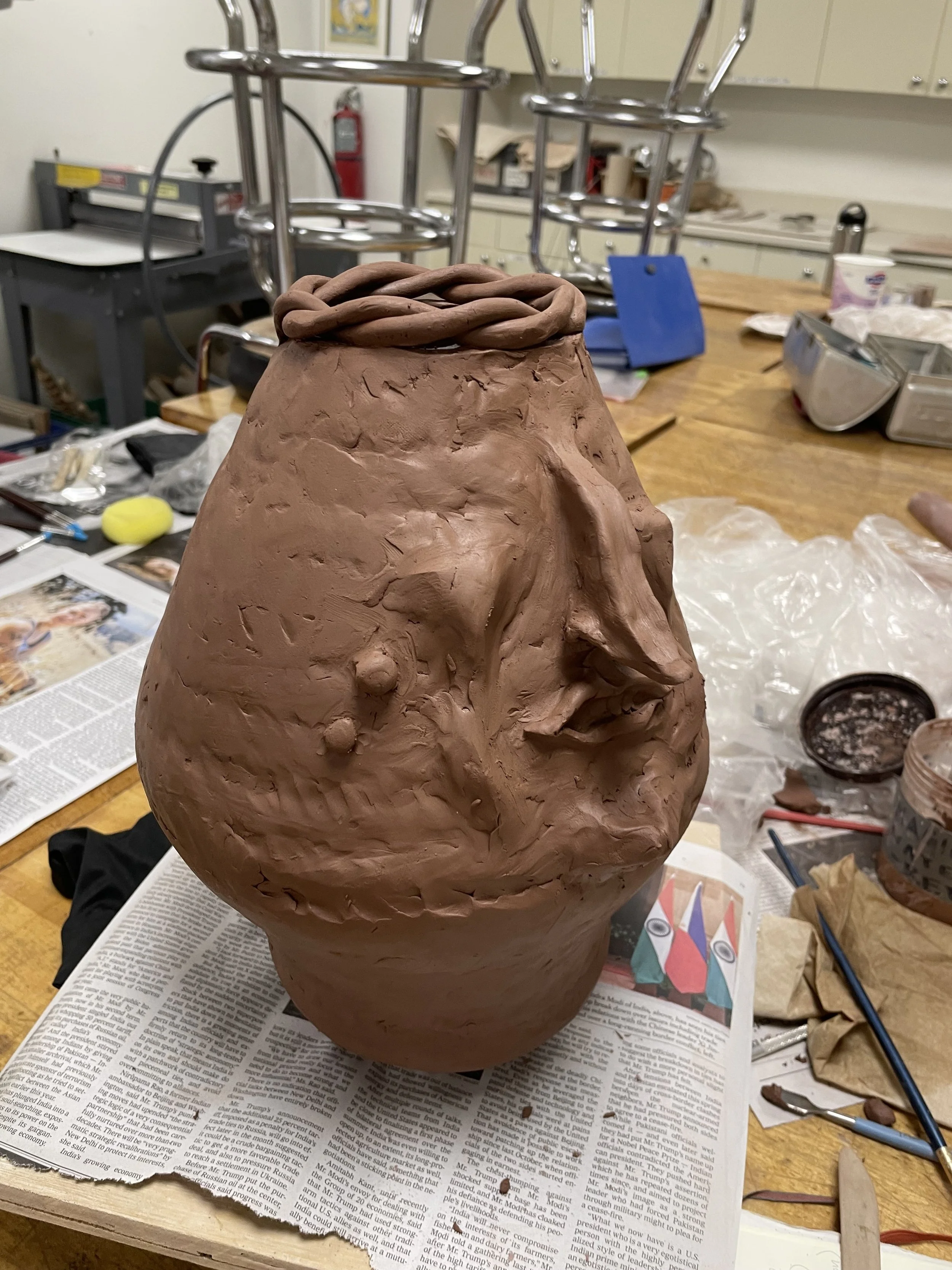 Two-handled vase with a face made out of reddish-brown clay, before it is fired in the kiln.
