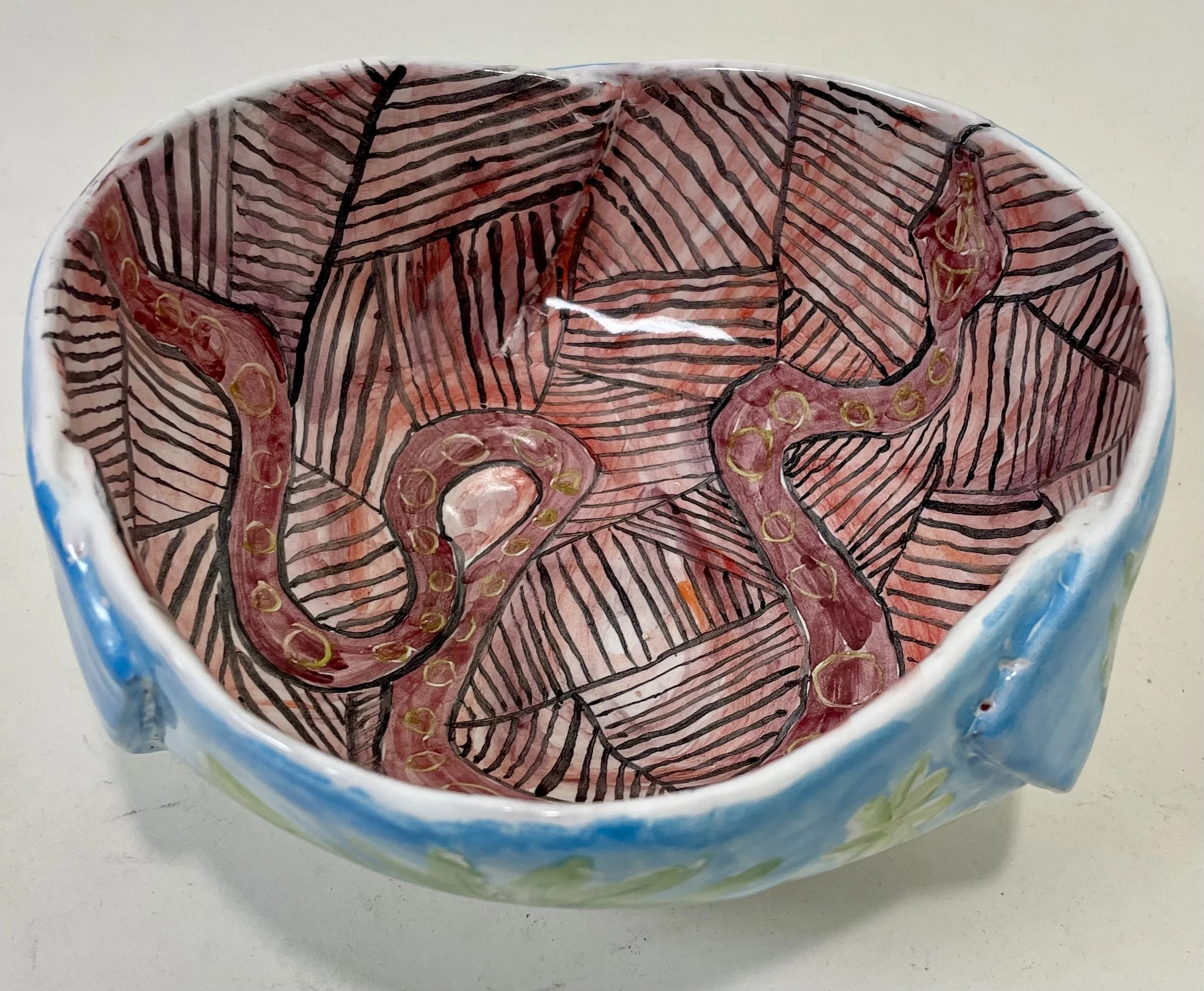 A ceramic bowl with a hand-painted interior design of pink snakes and black outlined leaves.