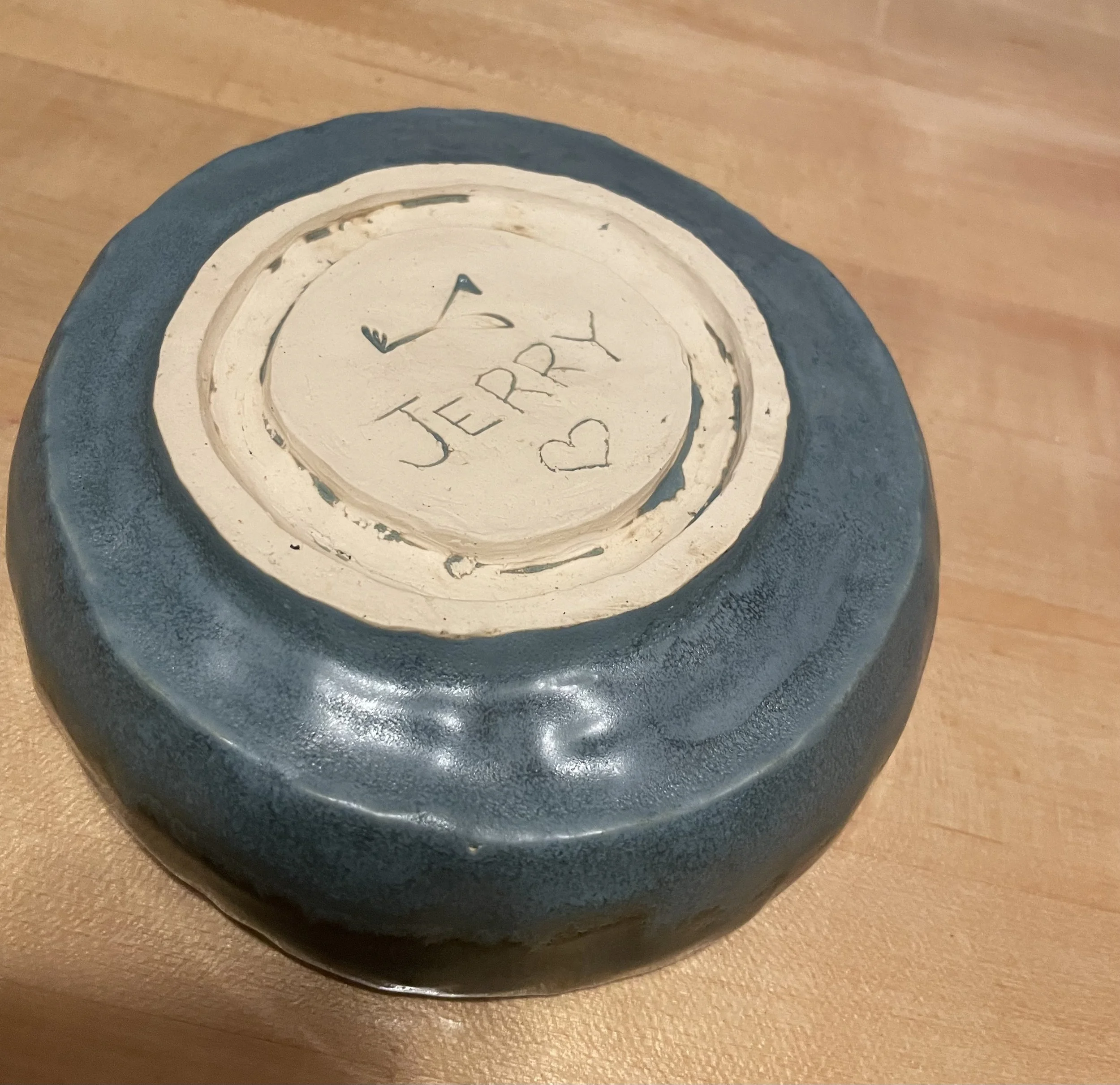 A ceramic bowl with a cream-colored bottom and black exterior, placed upside down. The bottom has the handwritten word 'JERRY' with a heart symbol.