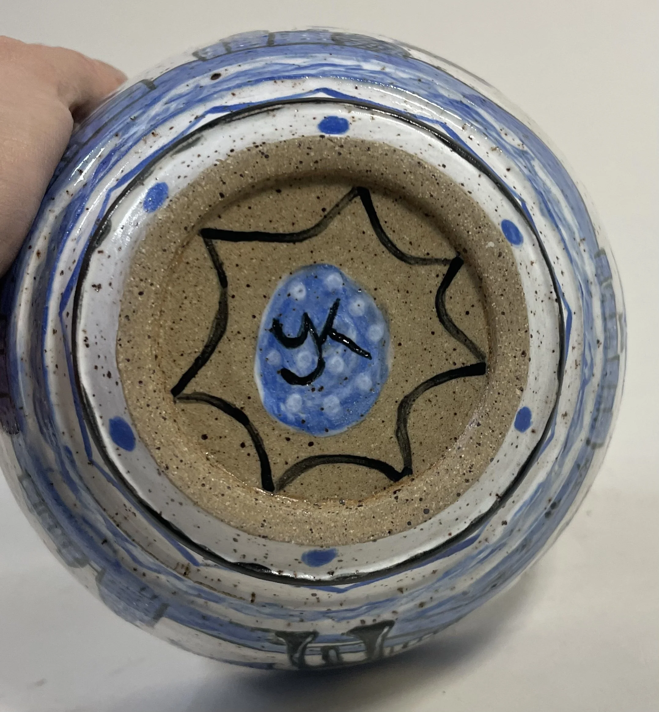 Underside of a hand-painted ceramic bowl with a beige and blue geometric pattern. A chop with the initials 'YK' is in the center inside a blue oval with white dots.