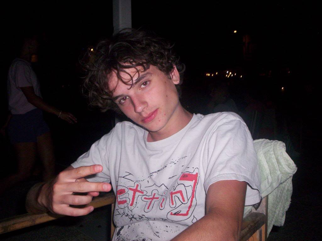 Archie Forde sitting on a chair looking badass. He is making a peace sign and wearing a red shirt.