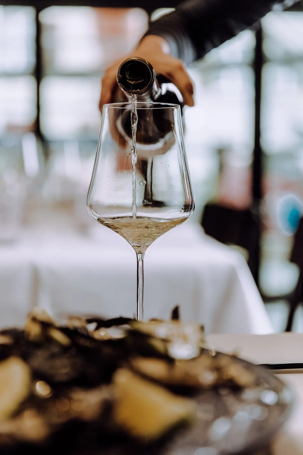 Person gießt Weißwein in ein Weinglas in einem Restaurant.