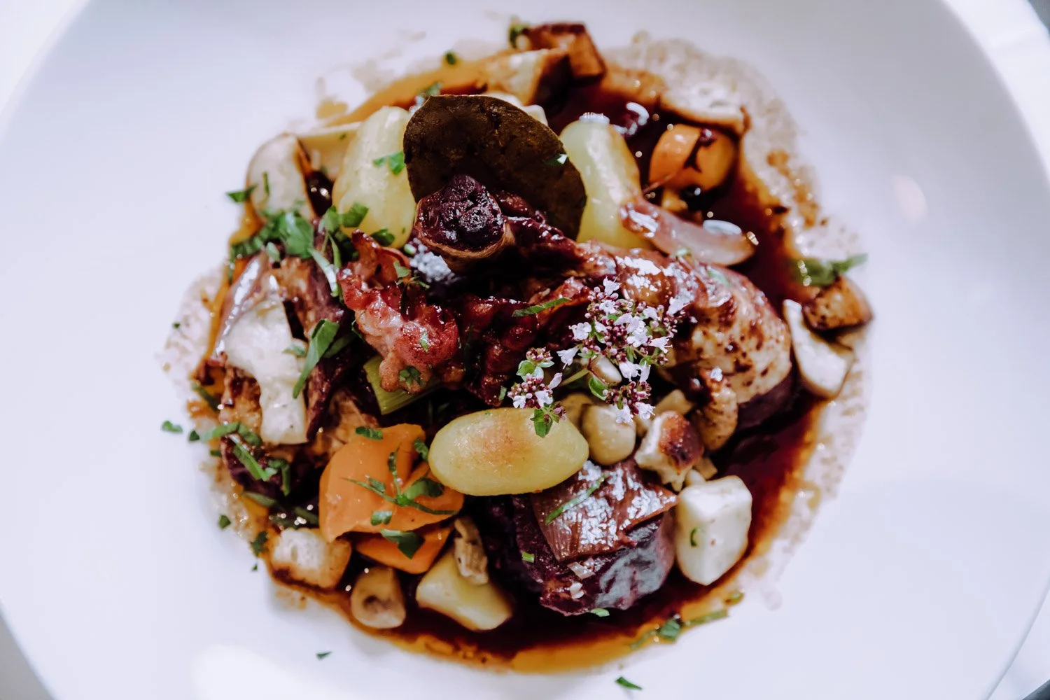 Ein kreatives Gericht mit Kartoffeln, Karotten, Fleisch, Pilzen und frischen Kräutern auf einem weißen Teller.